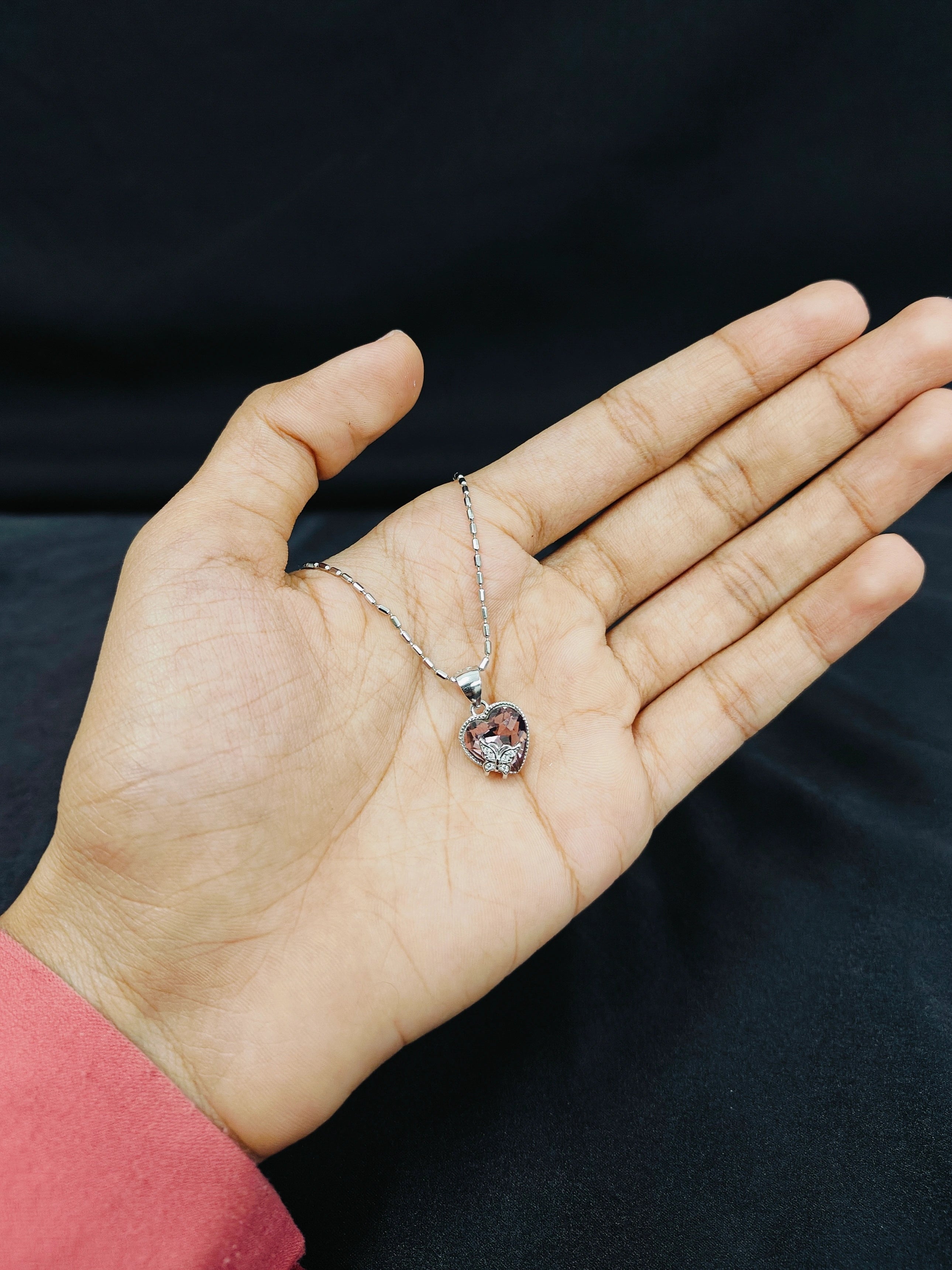 Hand holding a necklace with a pendant against a black background