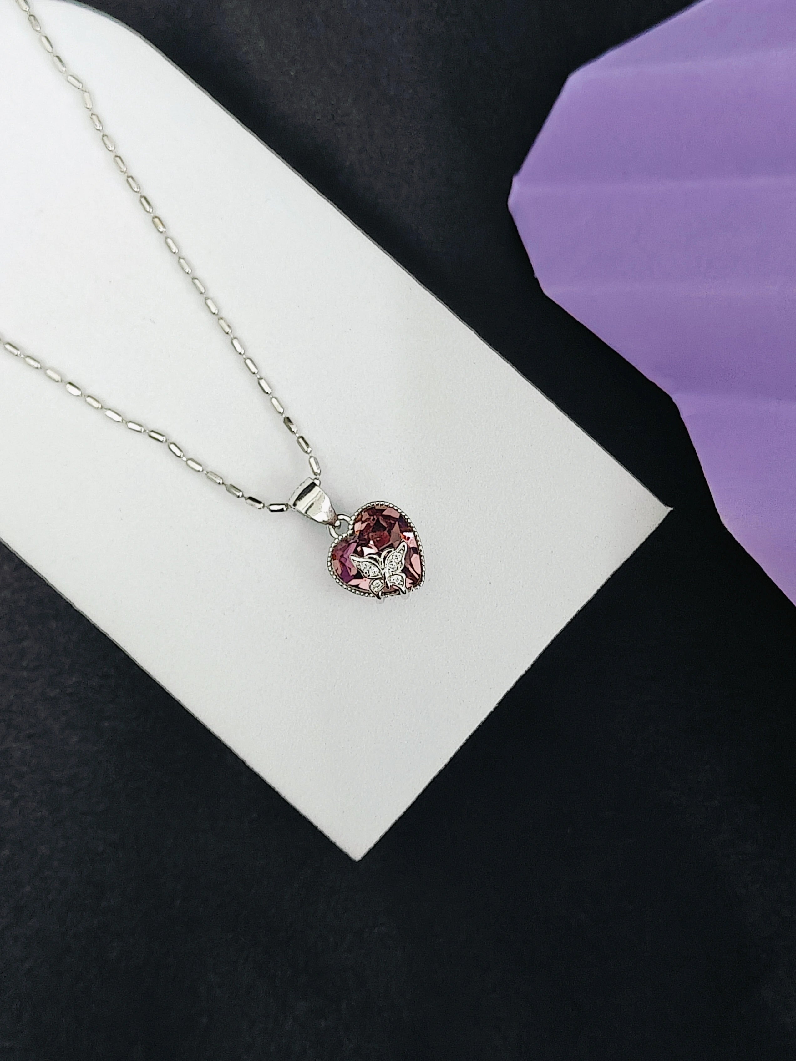 Heart-shaped pendant necklace on a white card with a purple background