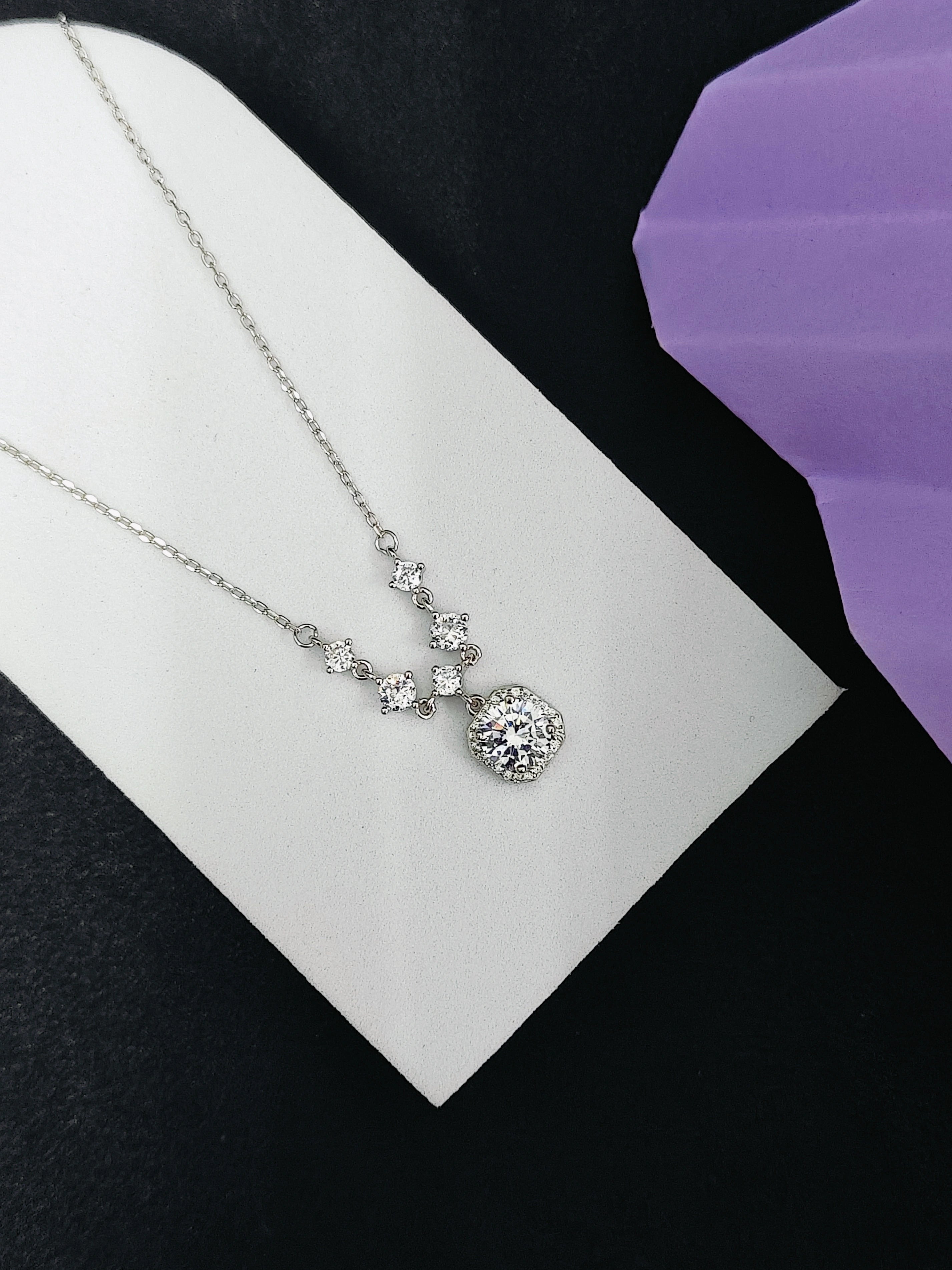 Silver necklace with a floral pendant on a white card against a black background