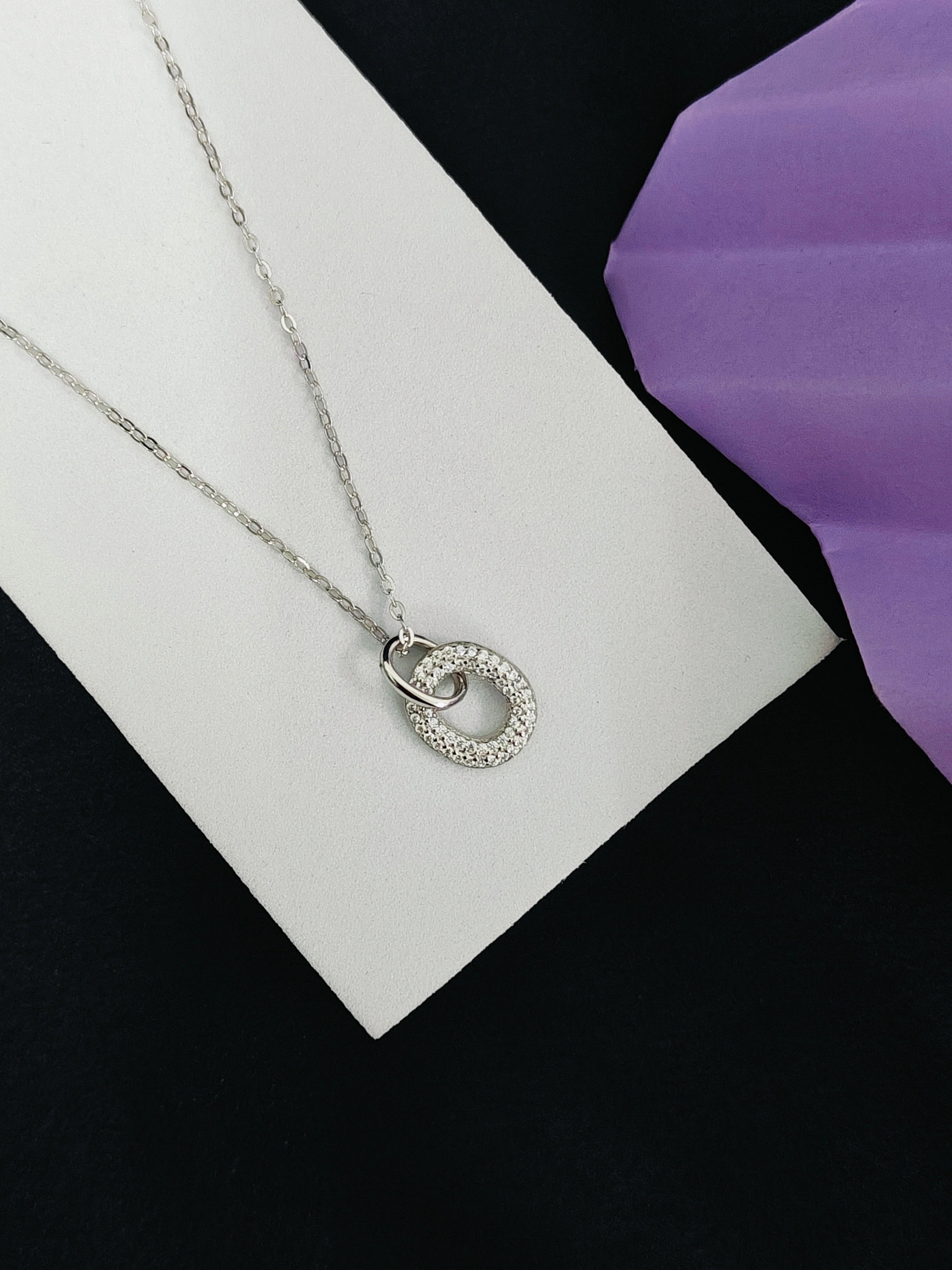 Silver necklace with a circular pendant on a white card with a purple flower.