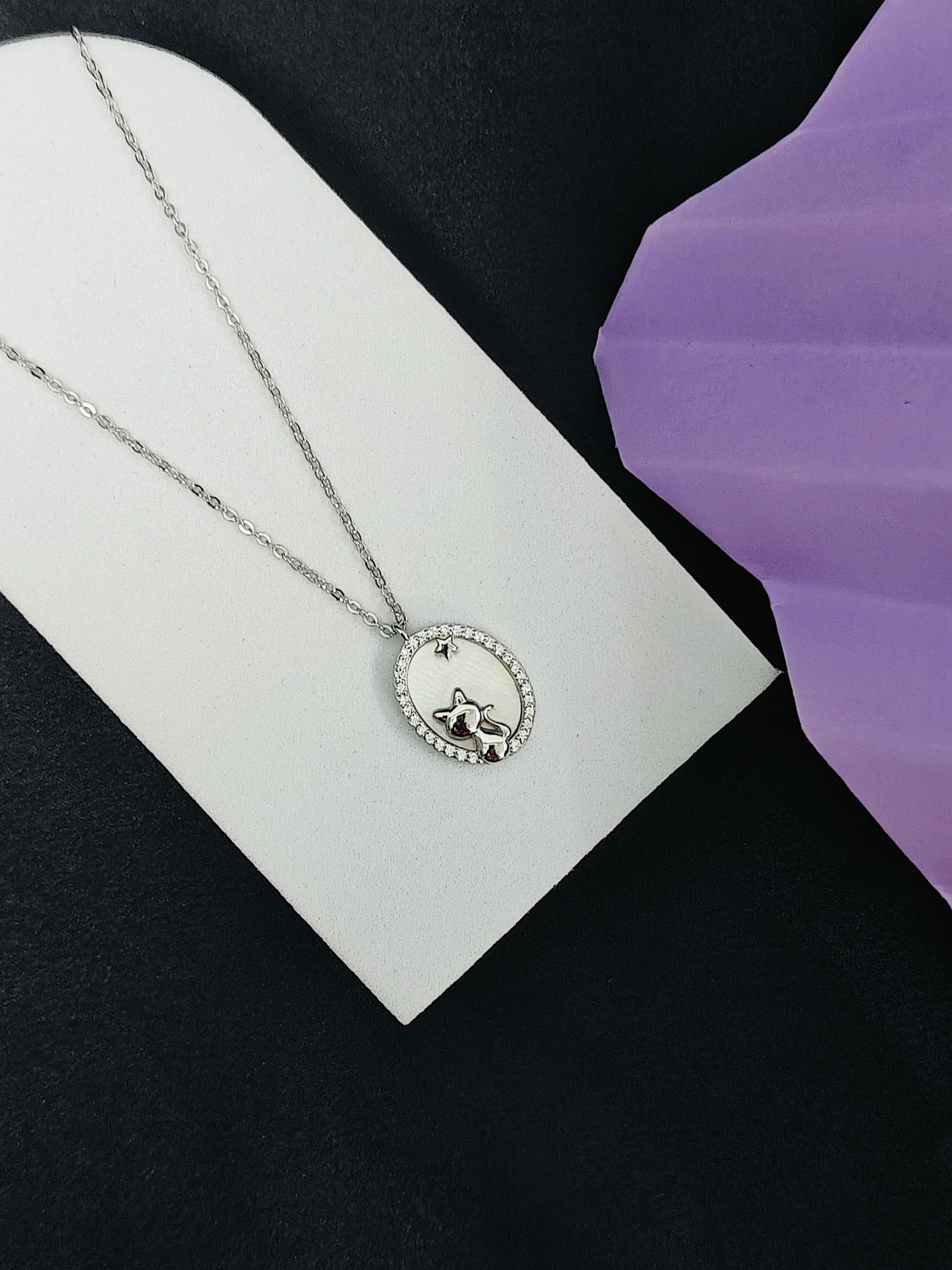 Silver necklace with a pendant on a white card against a black and purple background