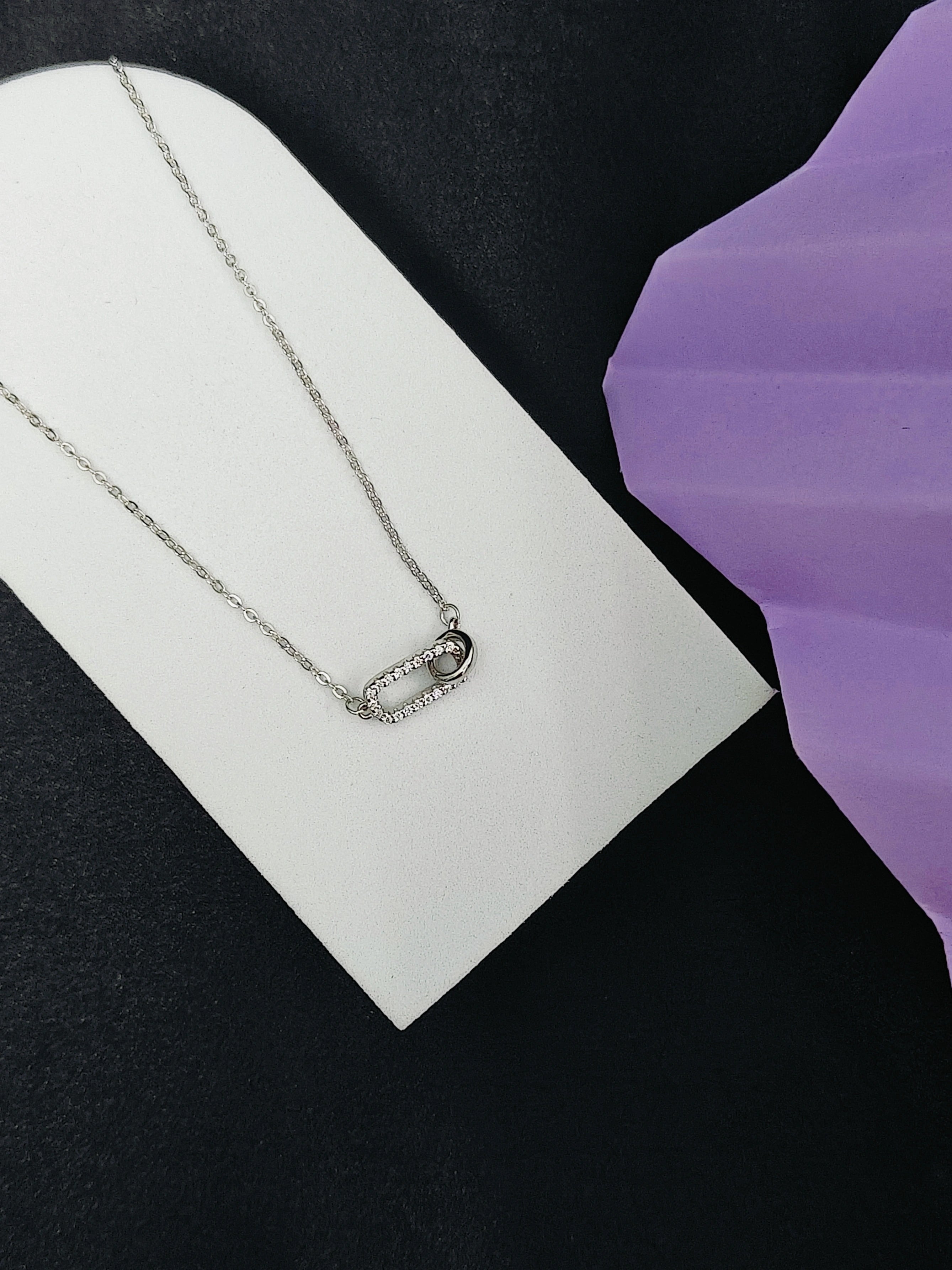 Silver necklace on a white card with a purple background