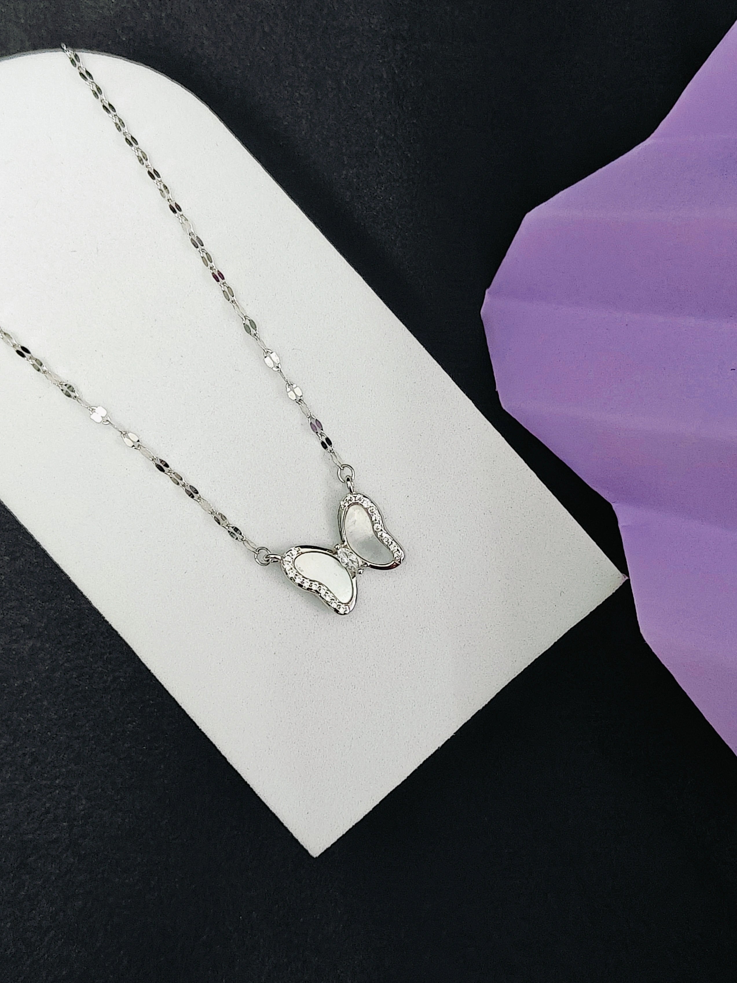 Silver butterfly necklace on a white card with a purple flower in the background
