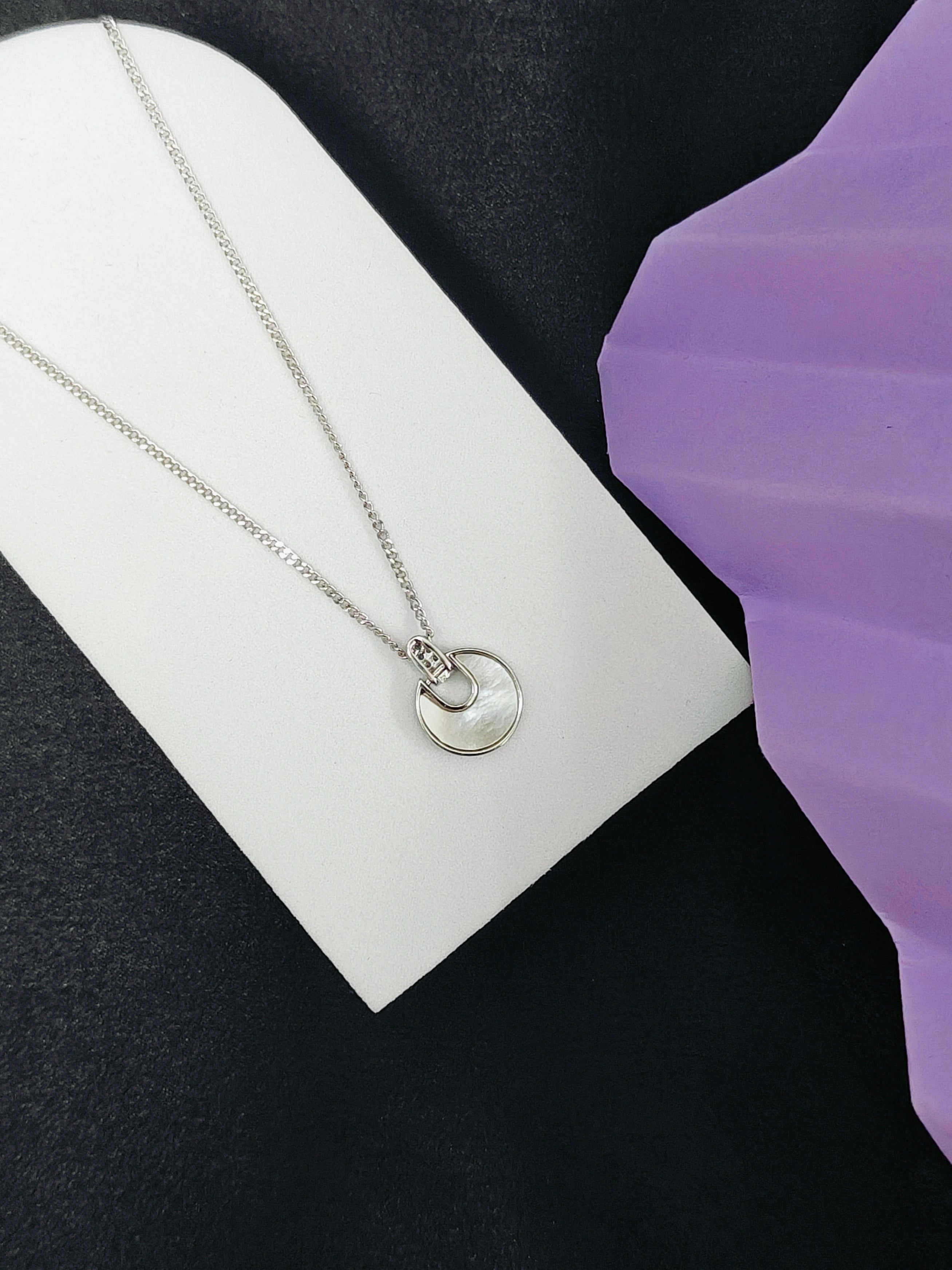 Silver necklace with a pendant on a white card against a black background