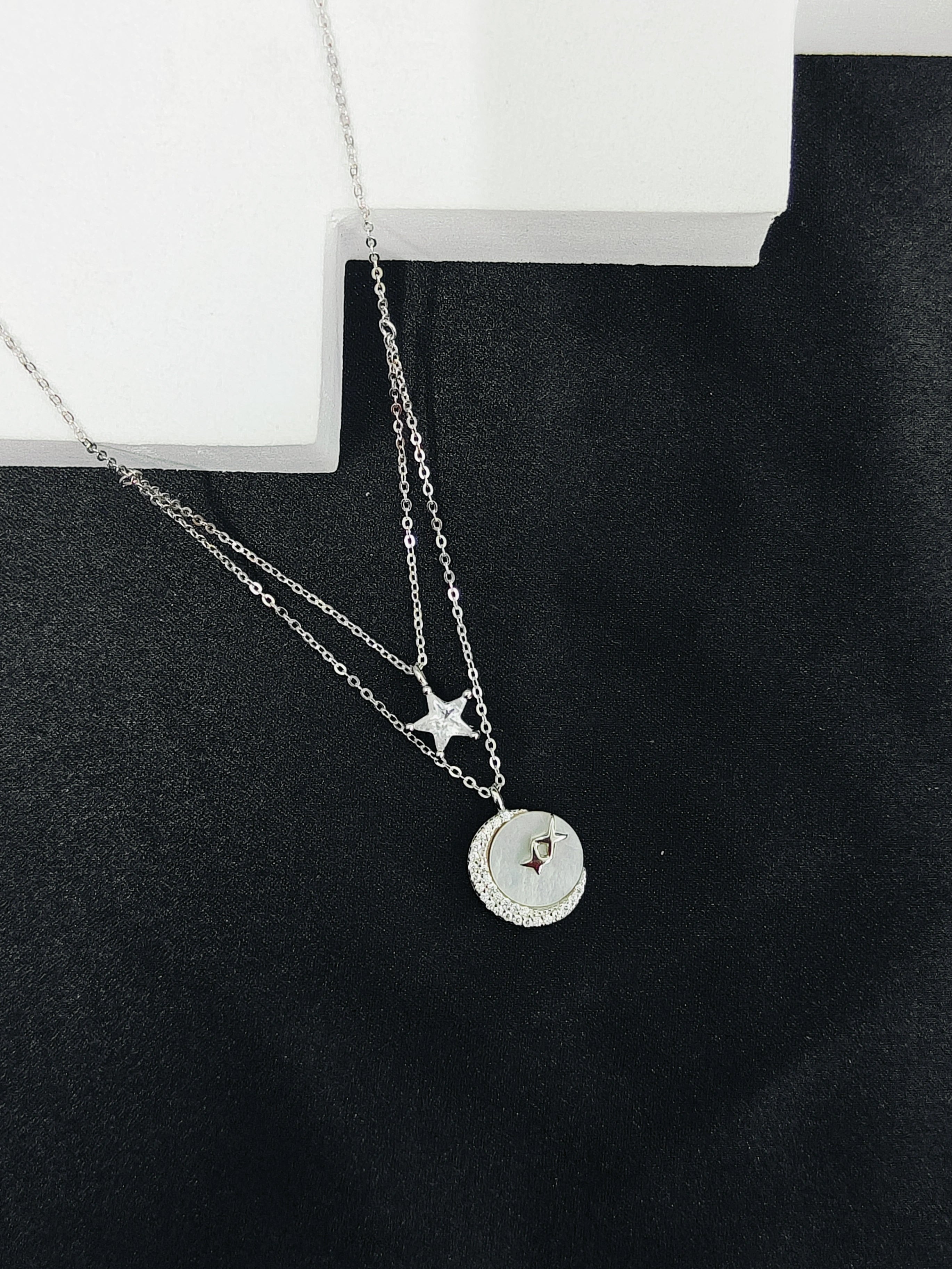 Silver necklace with star and round pendant on a black surface