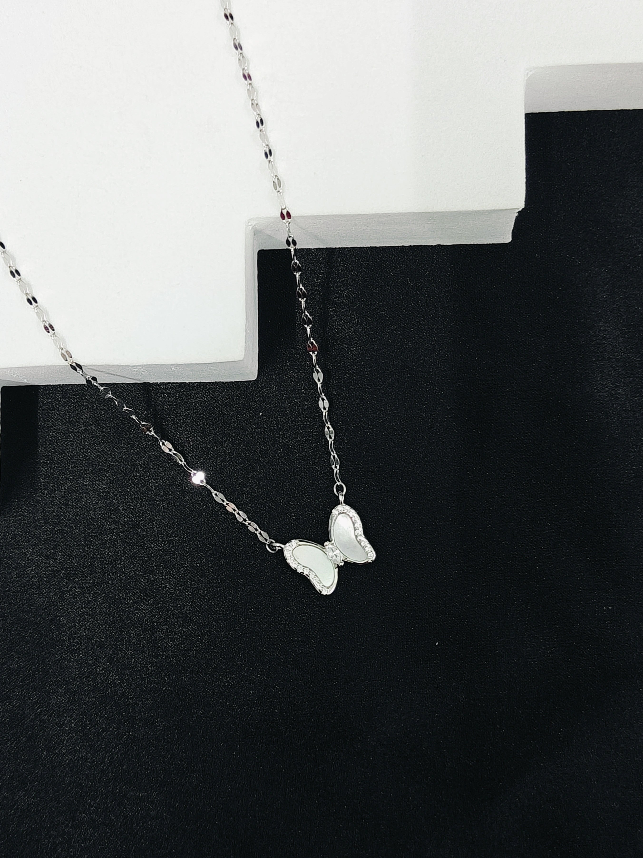 Butterfly necklace on a black stand with a white background