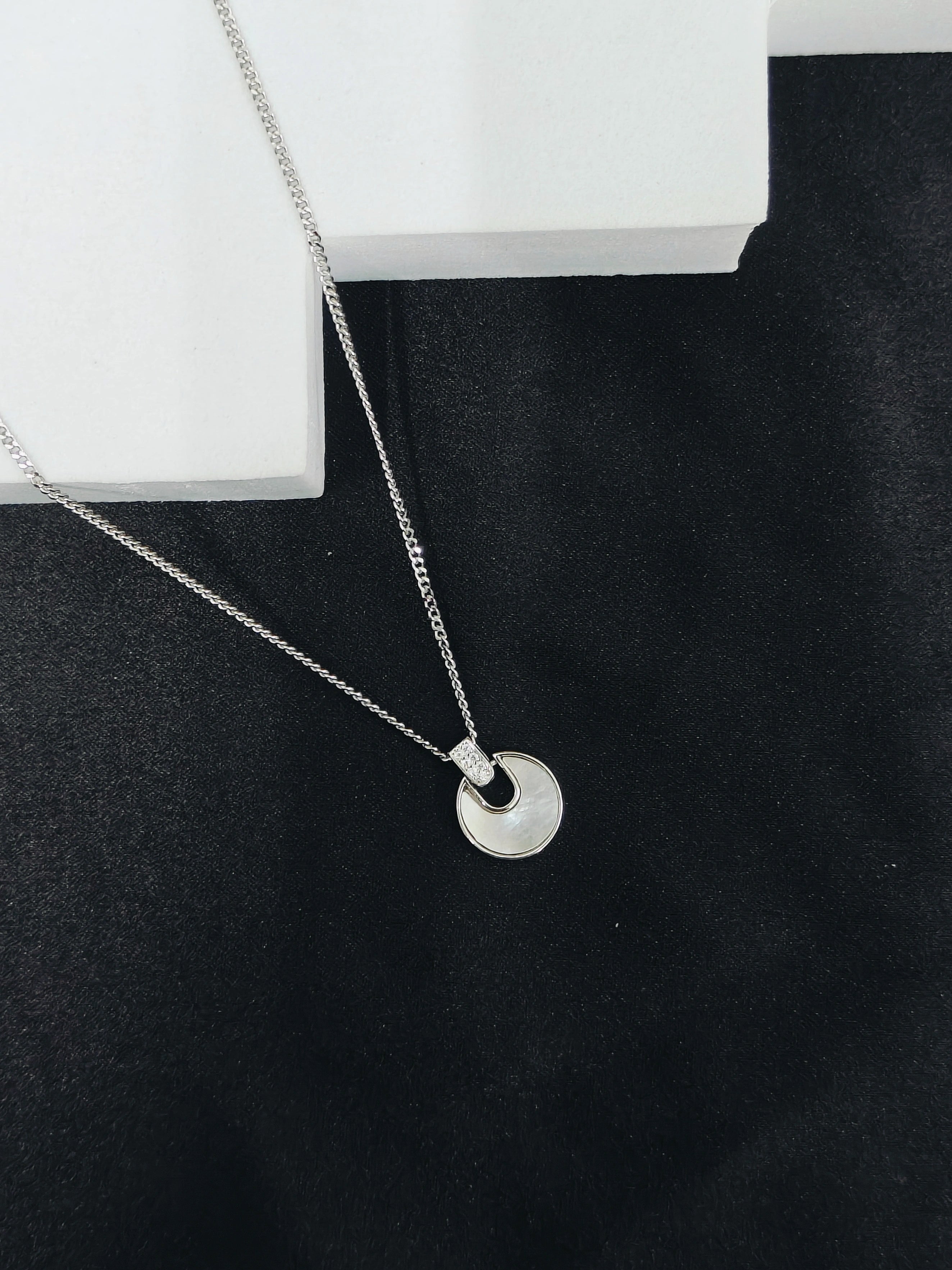 Silver necklace with a circular pendant on a black surface