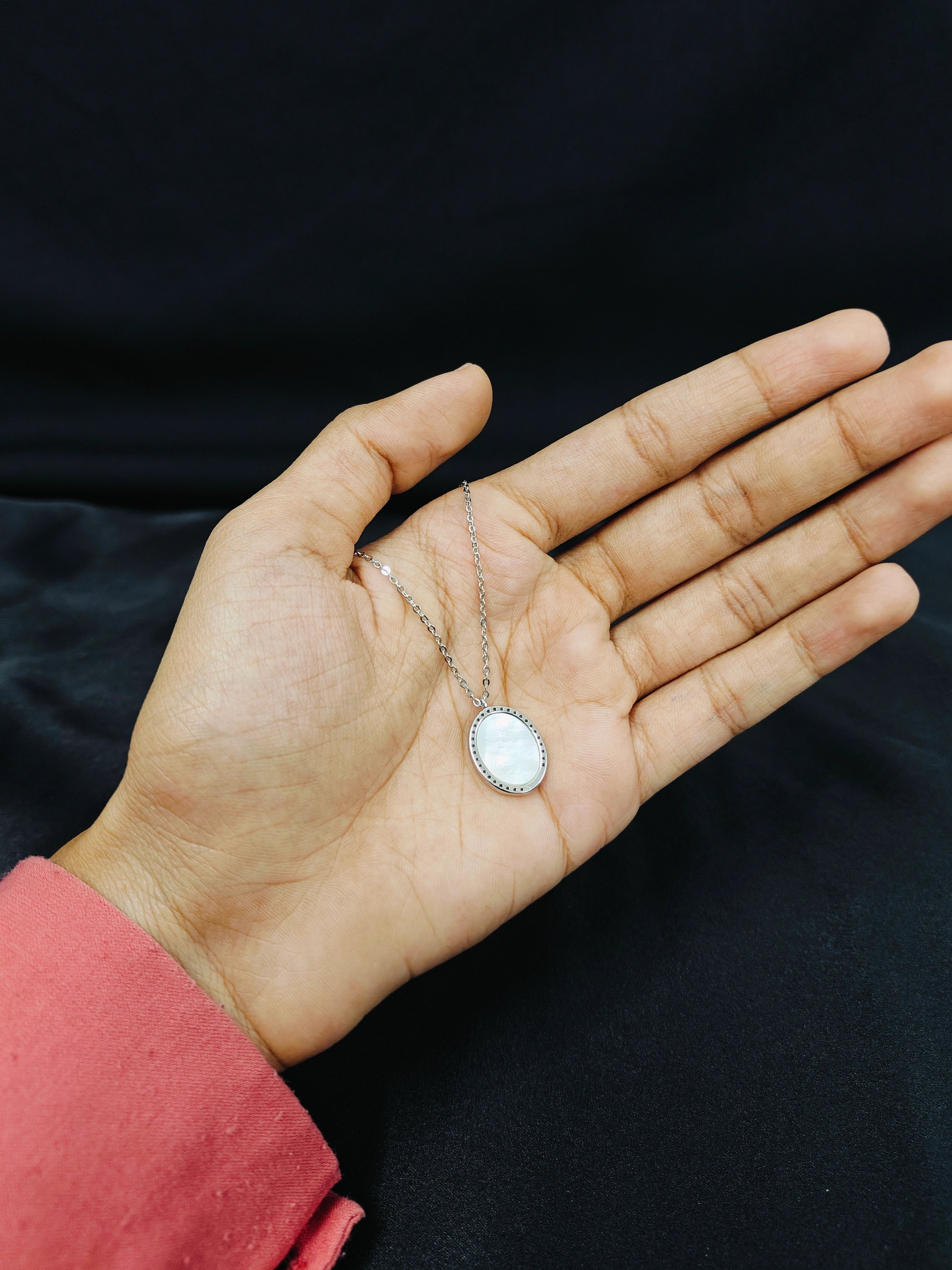 Hand holding a silver necklace with a round pendant against a black background