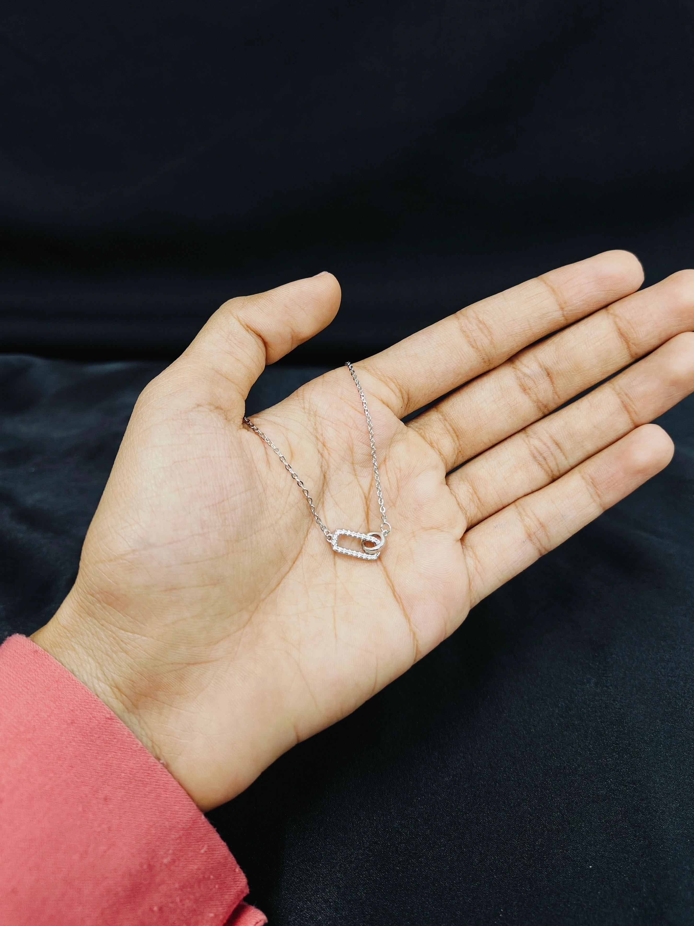 Hand holding a delicate necklace against a black background