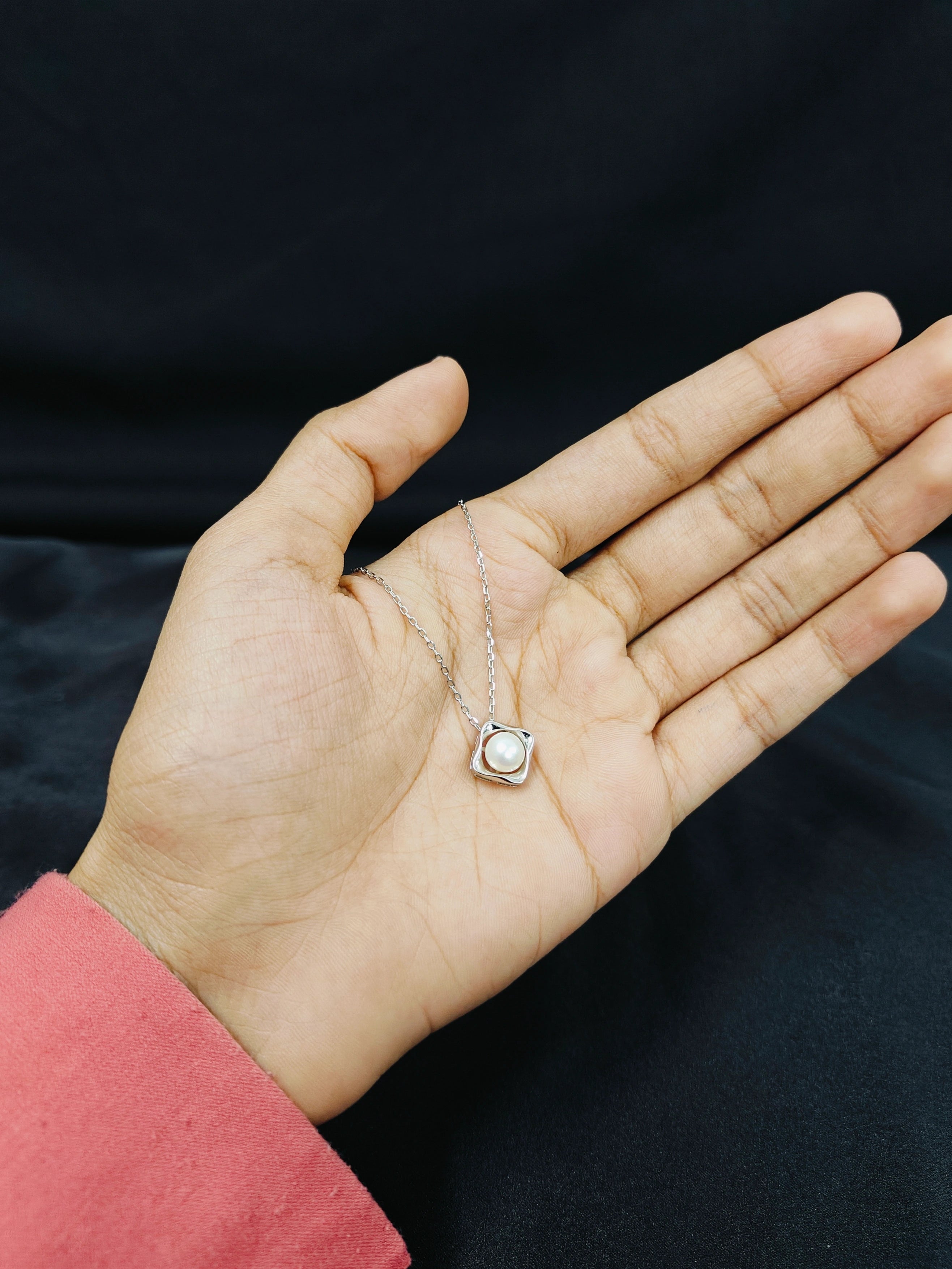 Hand holding a silver necklace with a pendant against a dark background