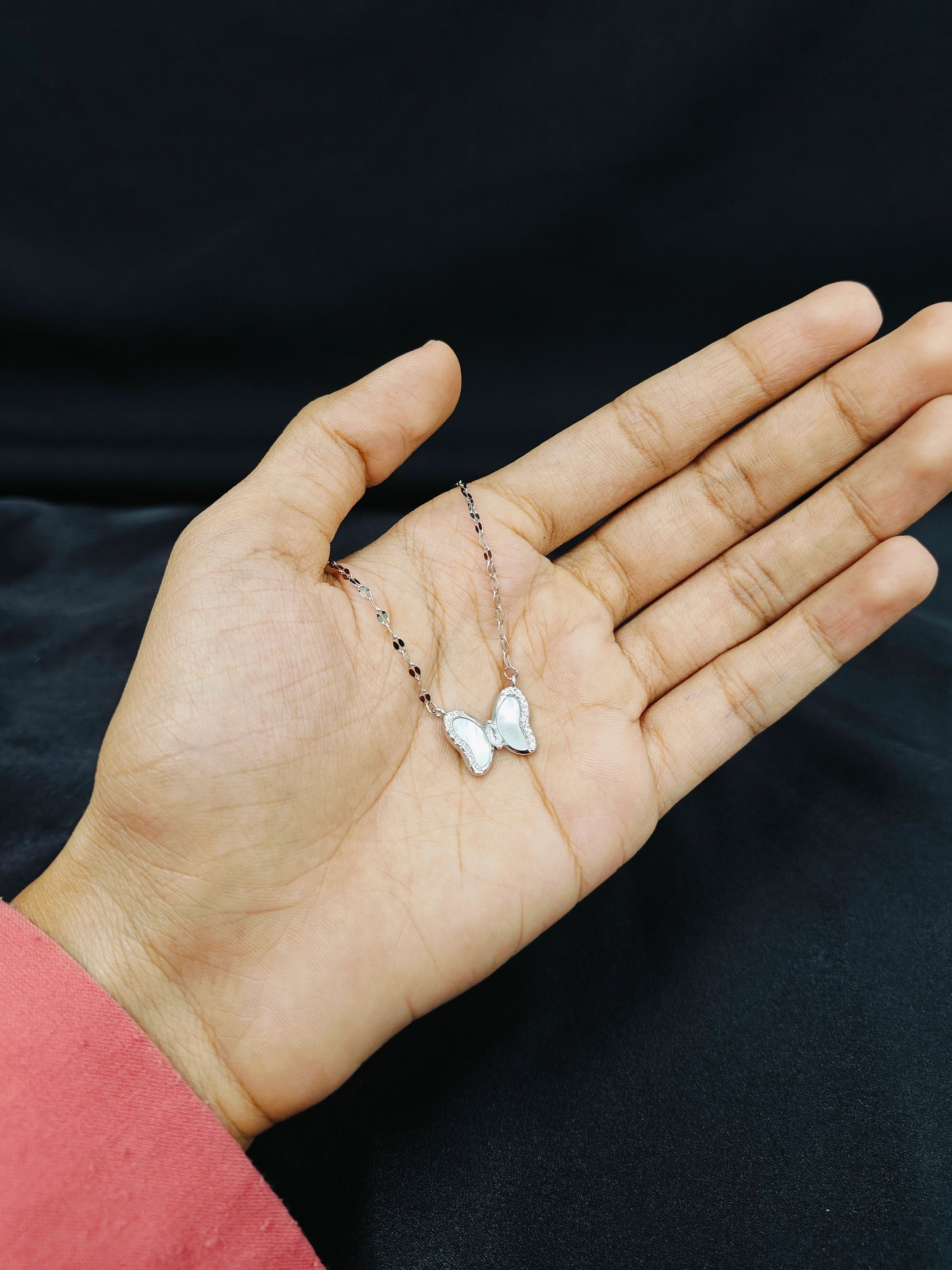Hand holding a delicate necklace with a butterfly pendant against a black background