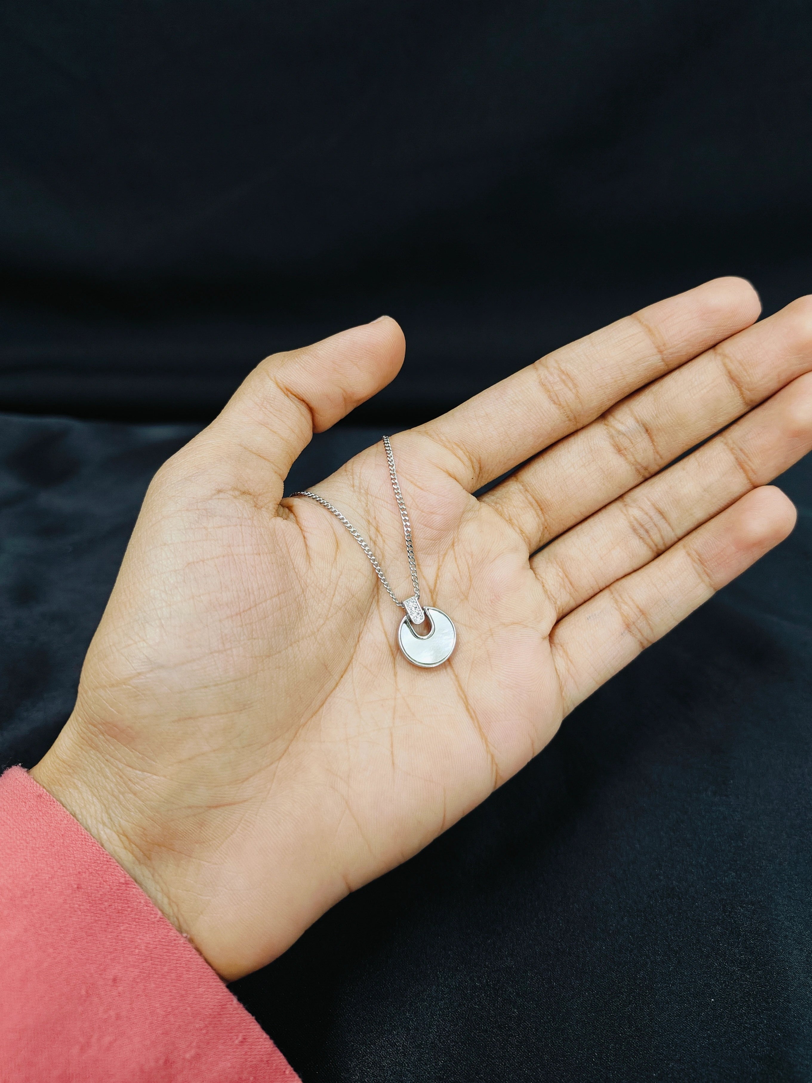 Hand holding a necklace with a small round pendant against a dark background