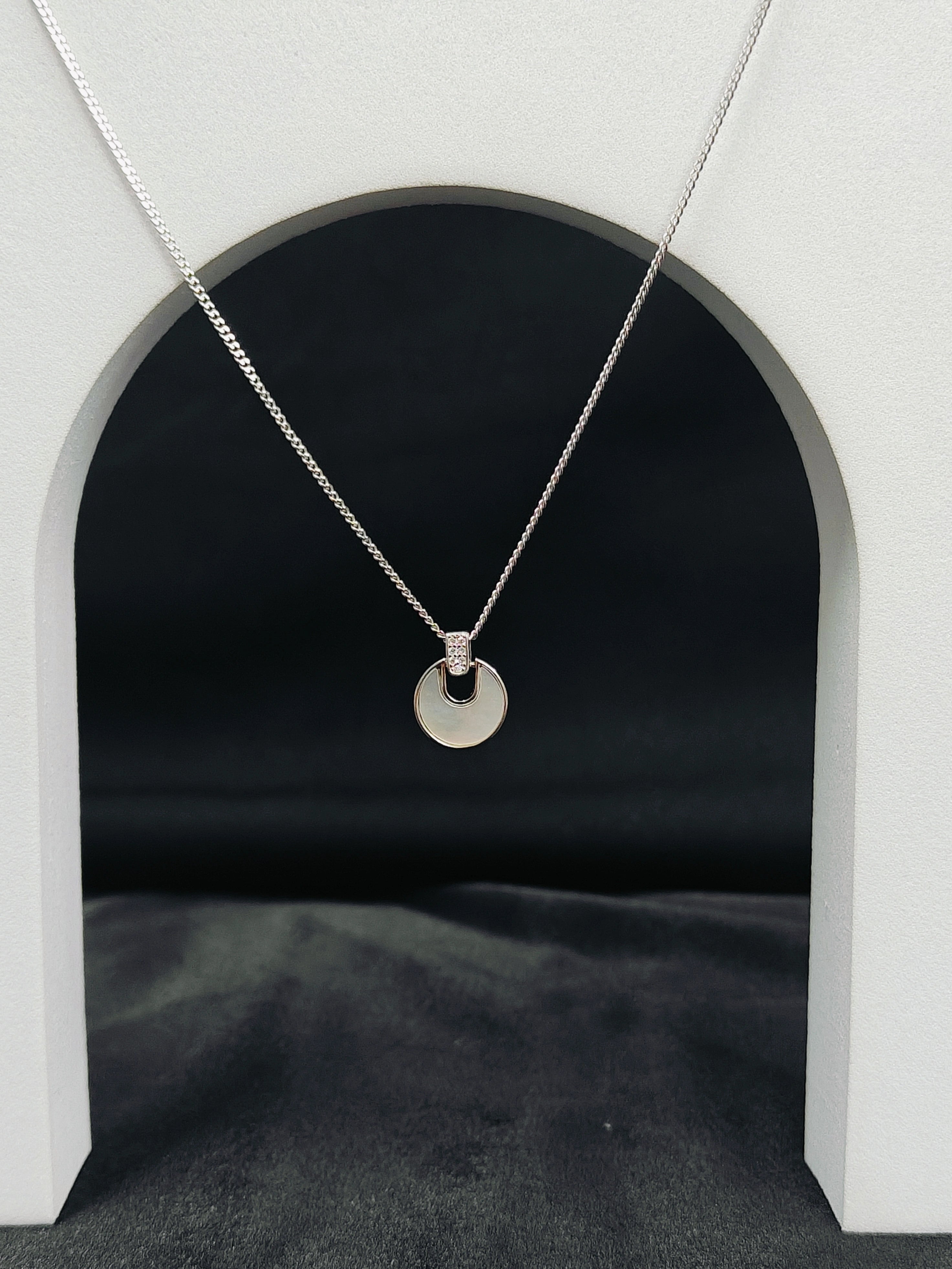Silver necklace with a round pendant on a black background