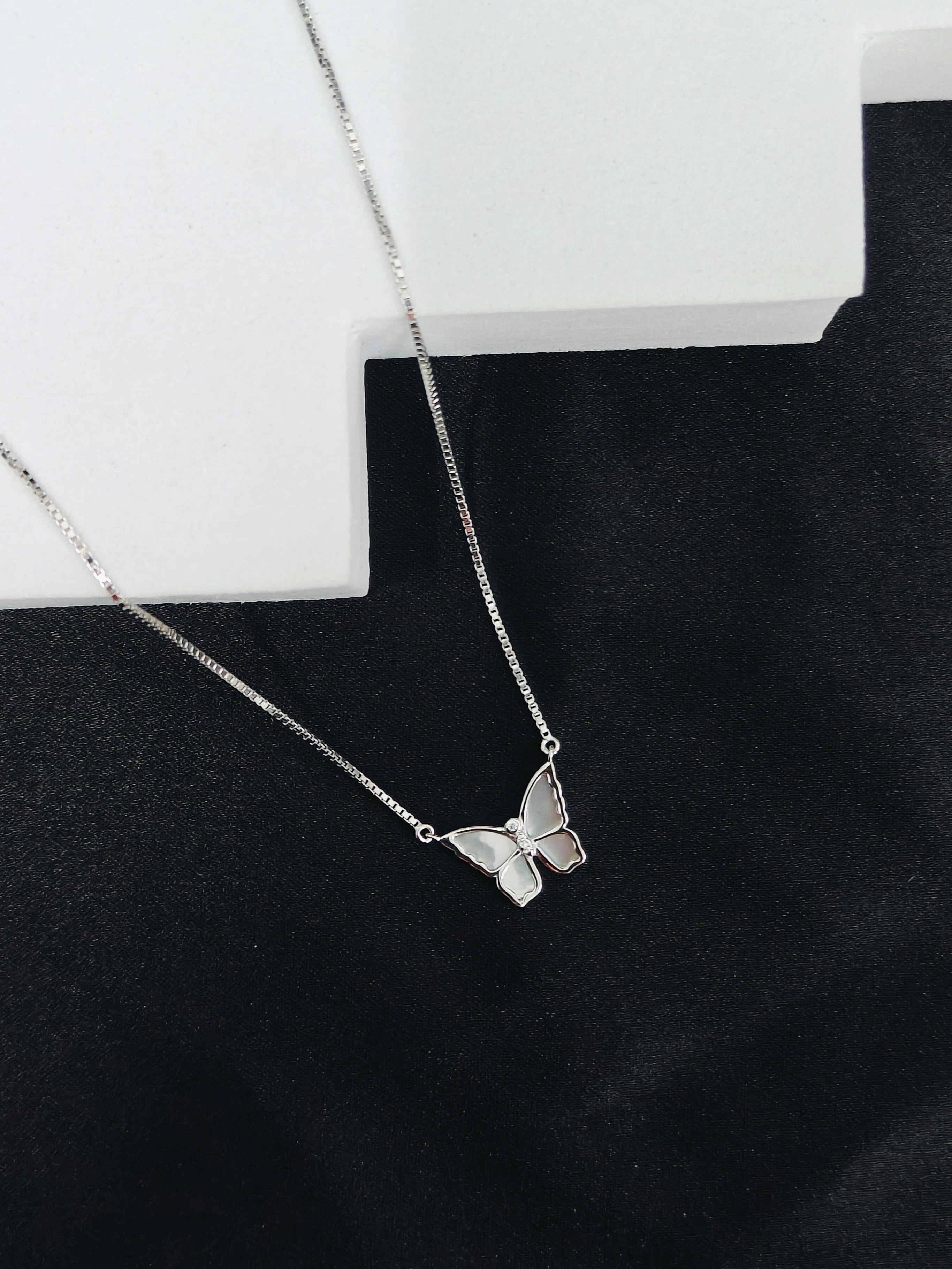 Silver butterfly necklace on a black surface with a white box in the background