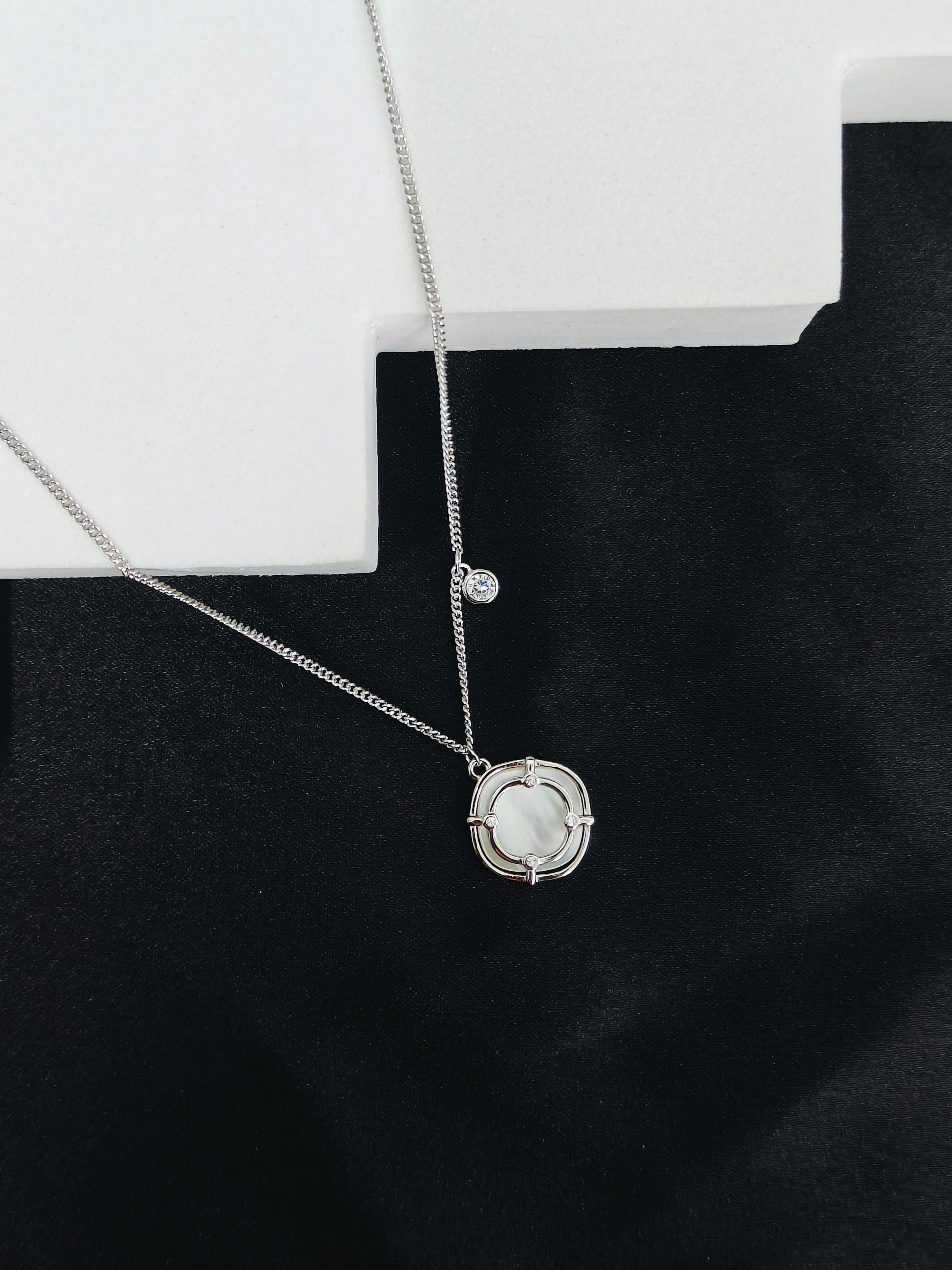 Silver necklace with a circular pendant on a black background