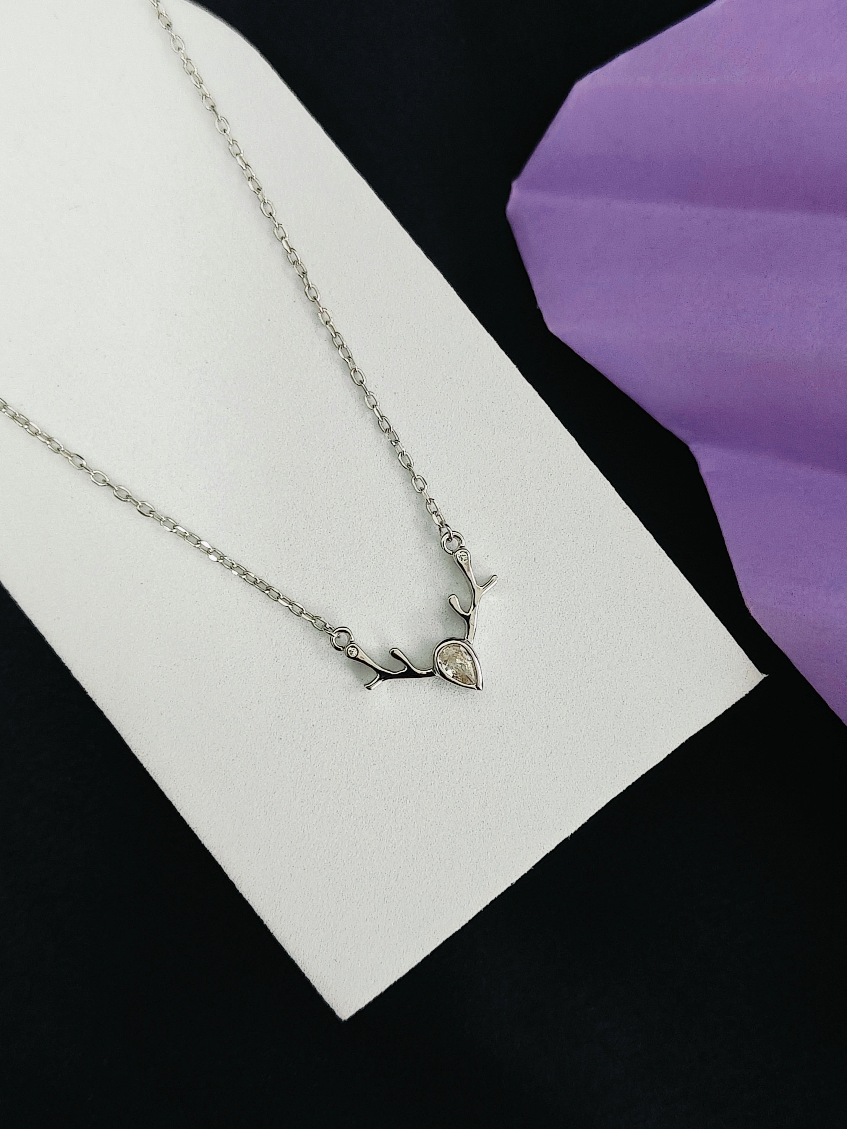 Silver necklace with a heart pendant on a white card with a purple flower in the background