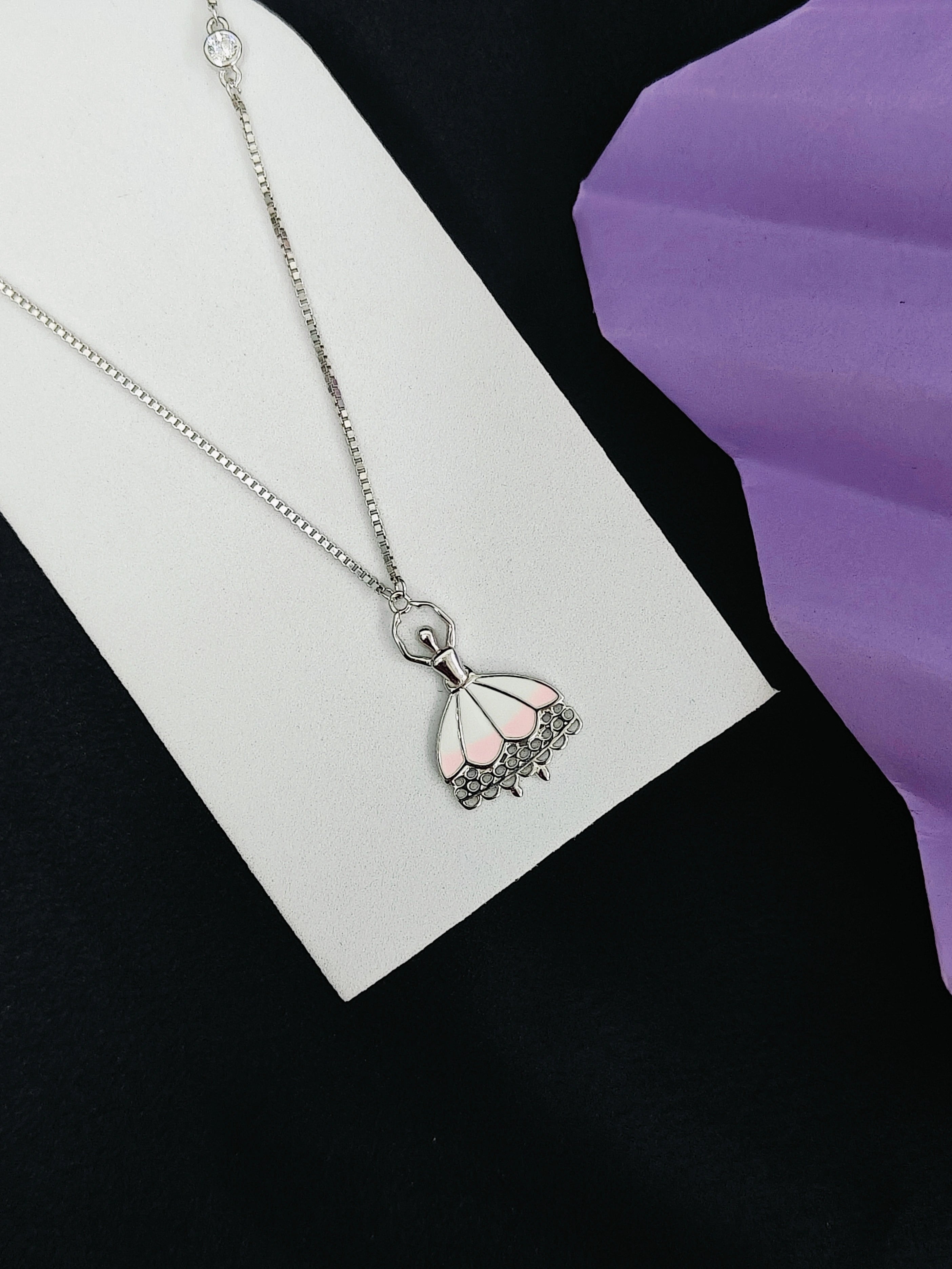 Necklace with a pink and black pendant on a white card against a purple background