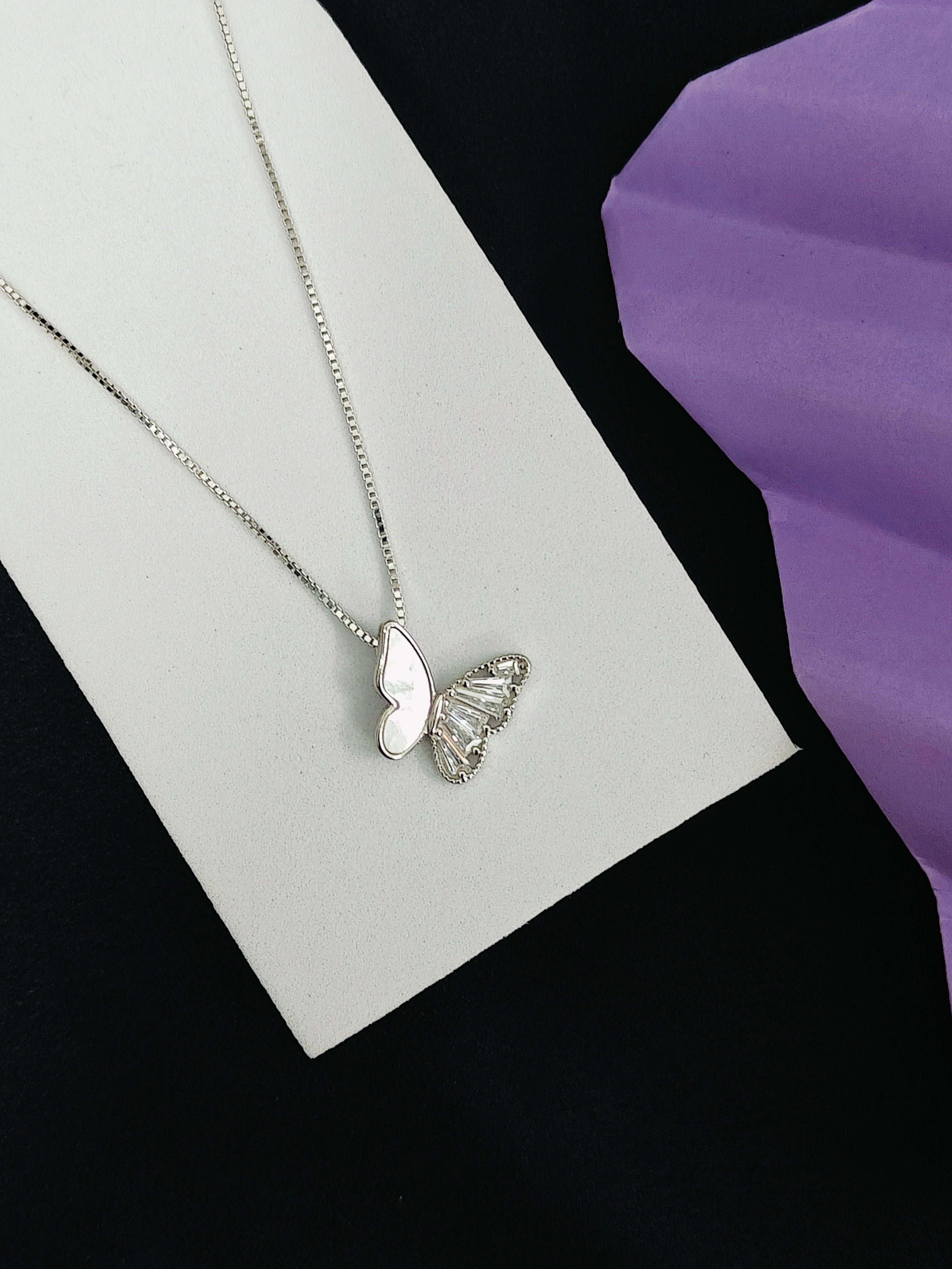 Butterfly-shaped silver pendant on a necklace against a black and purple background