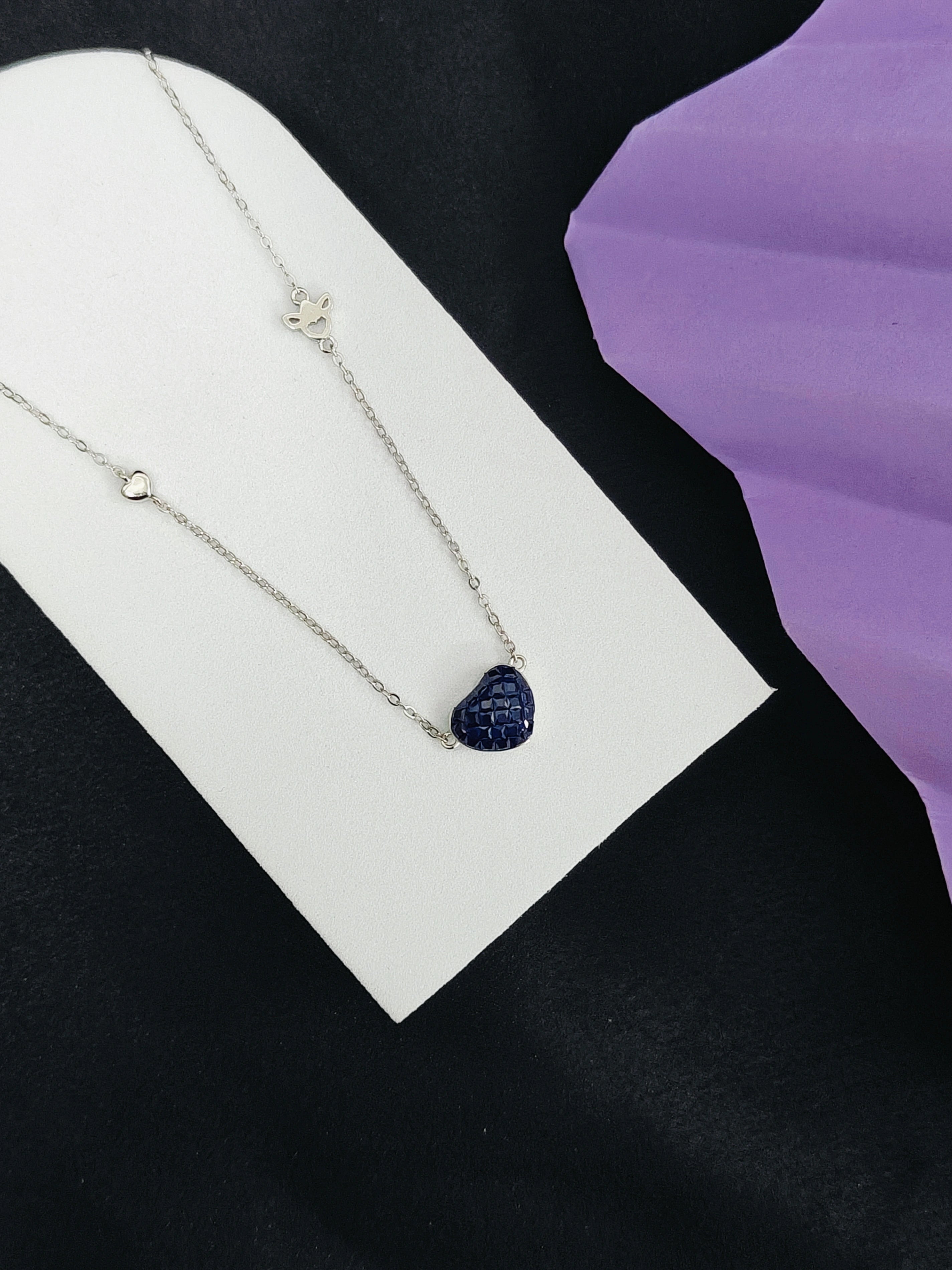Necklace with a heart-shaped pendant on a white card against a black and purple background