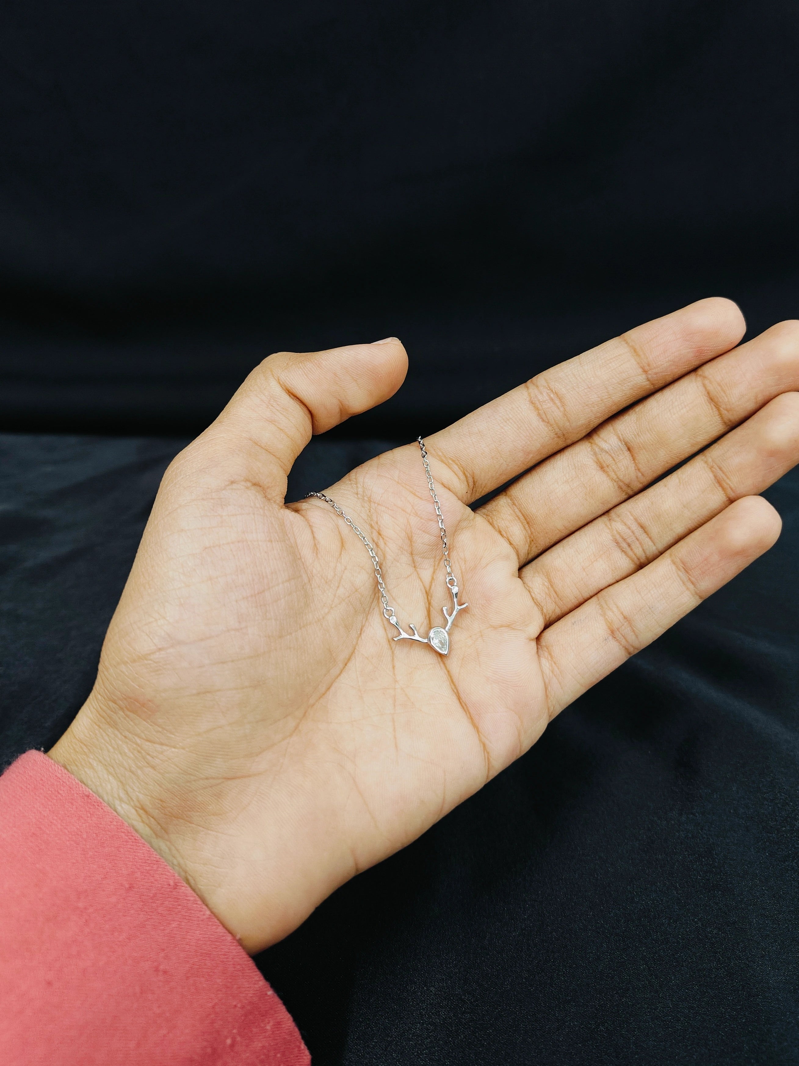 Hand holding a delicate silver necklace against a black background
