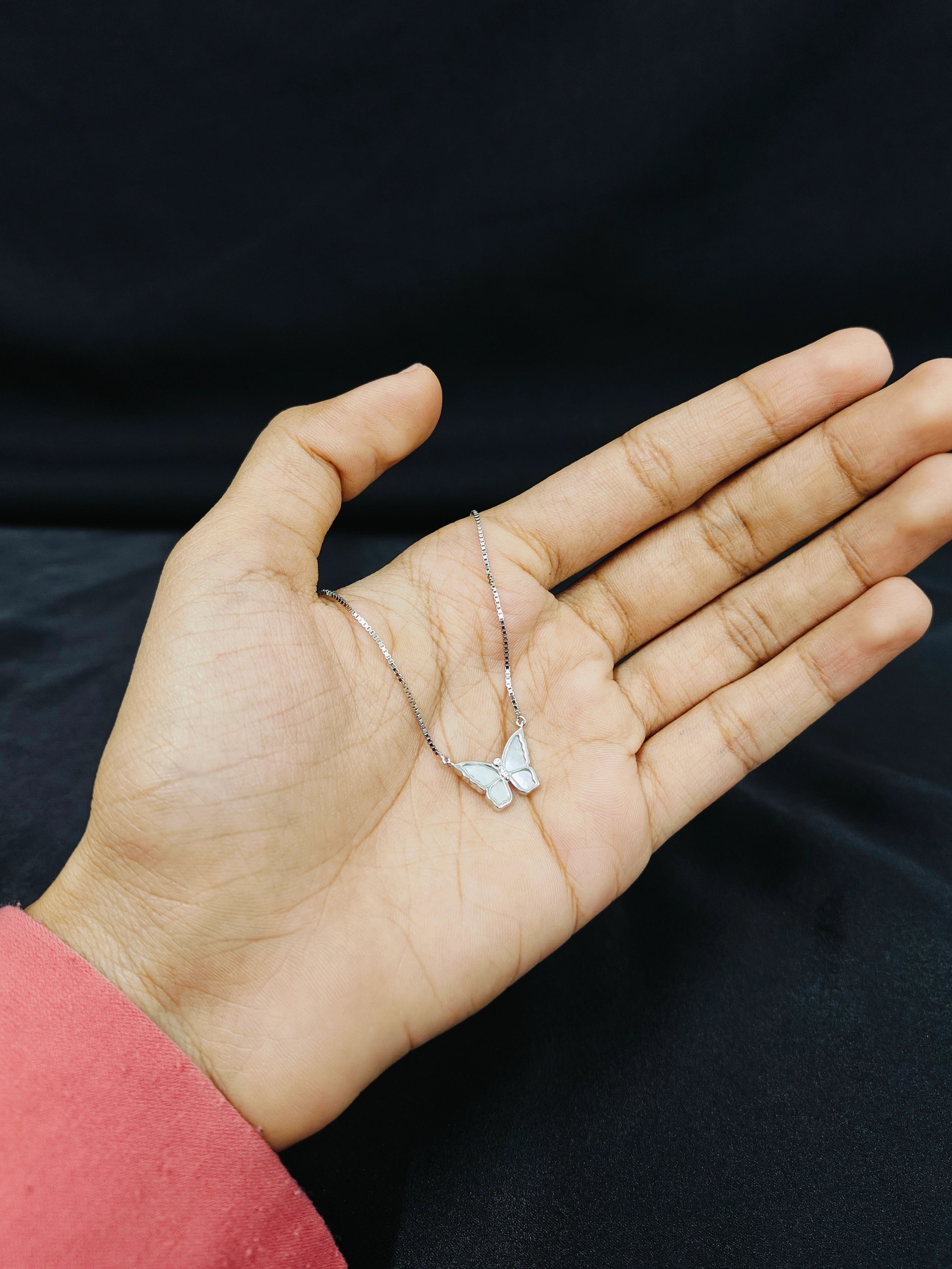 Butterfly necklace held in a hand against a black background