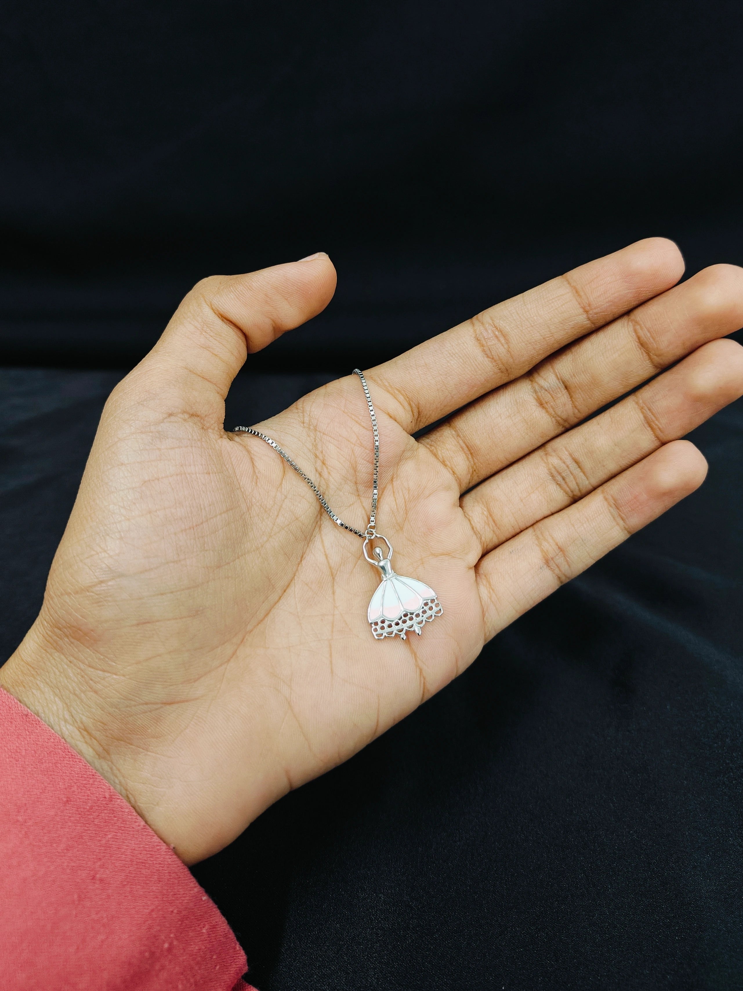 Hand holding a silver necklace with a heart-shaped pendant against a black background