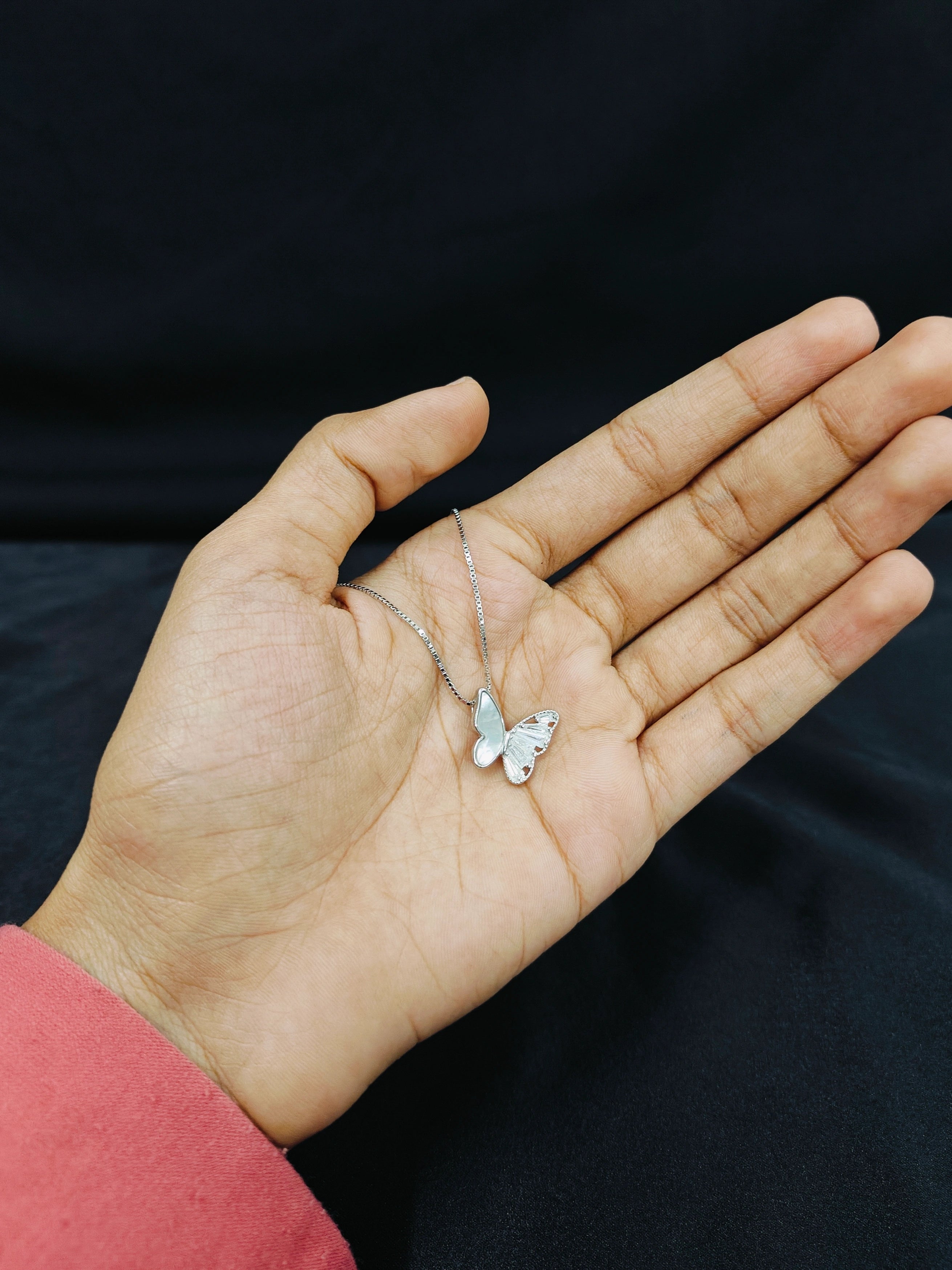 Hand holding a butterfly necklace against a black background