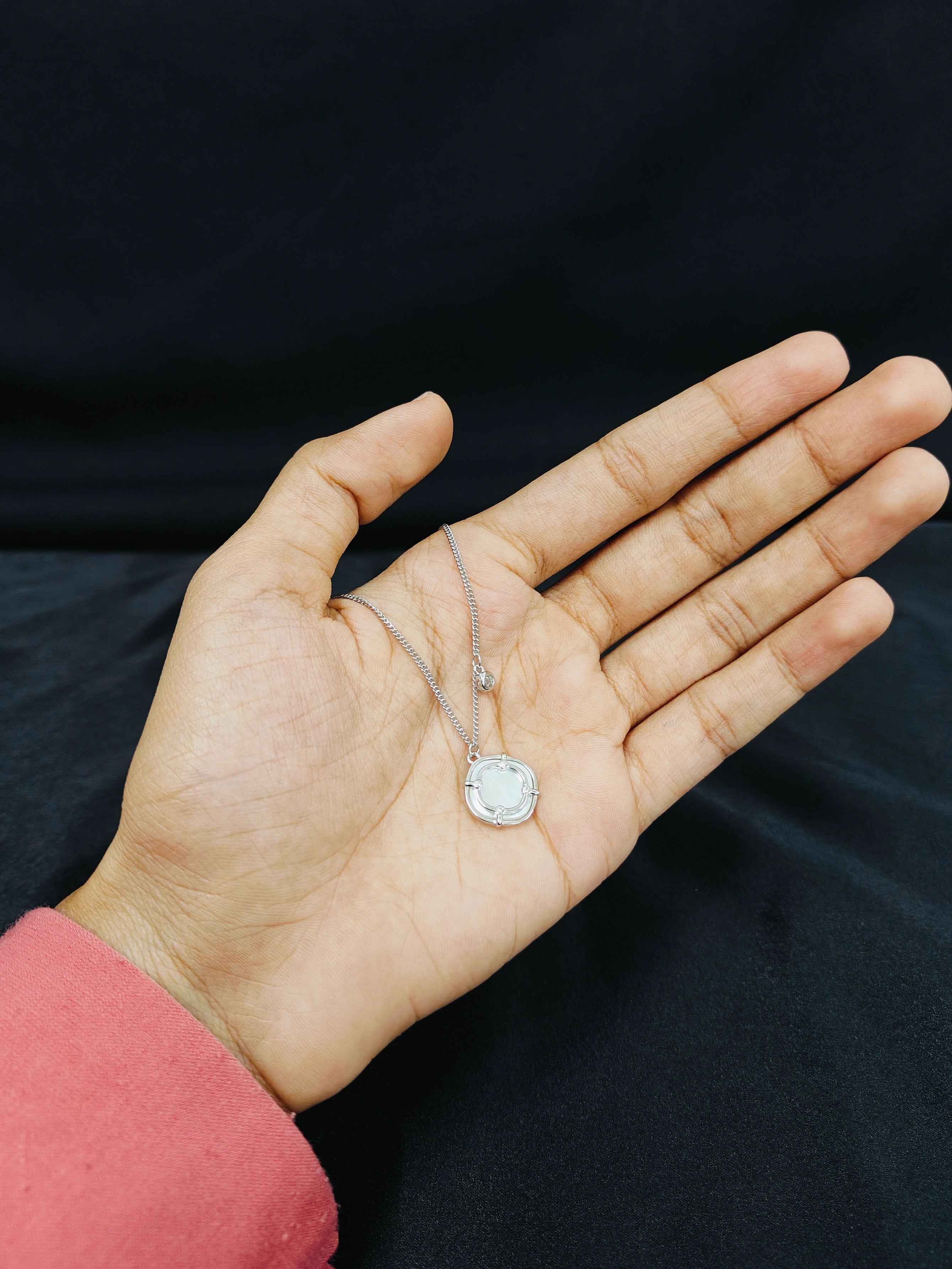 Hand holding a necklace with a pendant against a black background