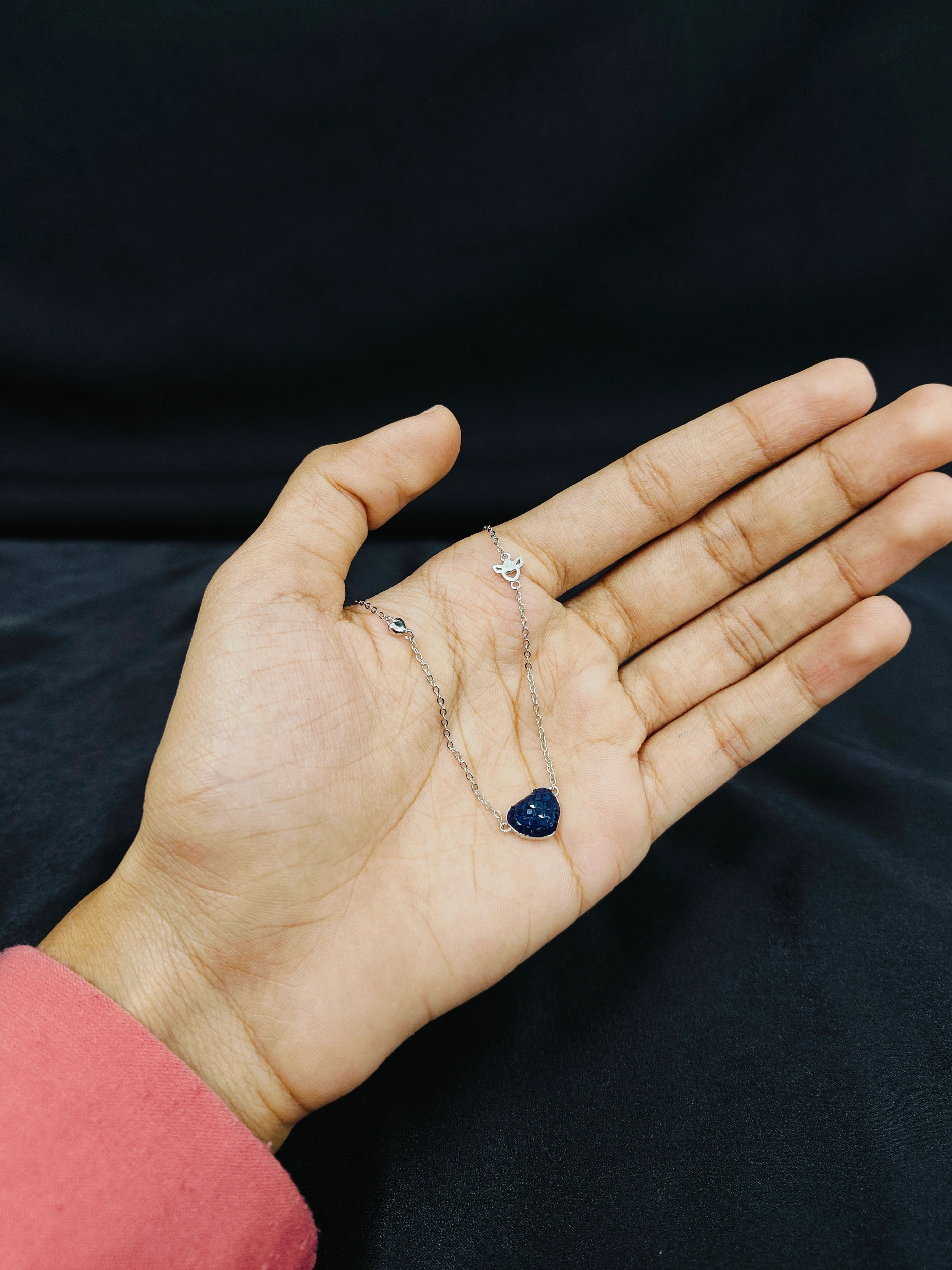 Hand holding a necklace with a blue pendant against a black background