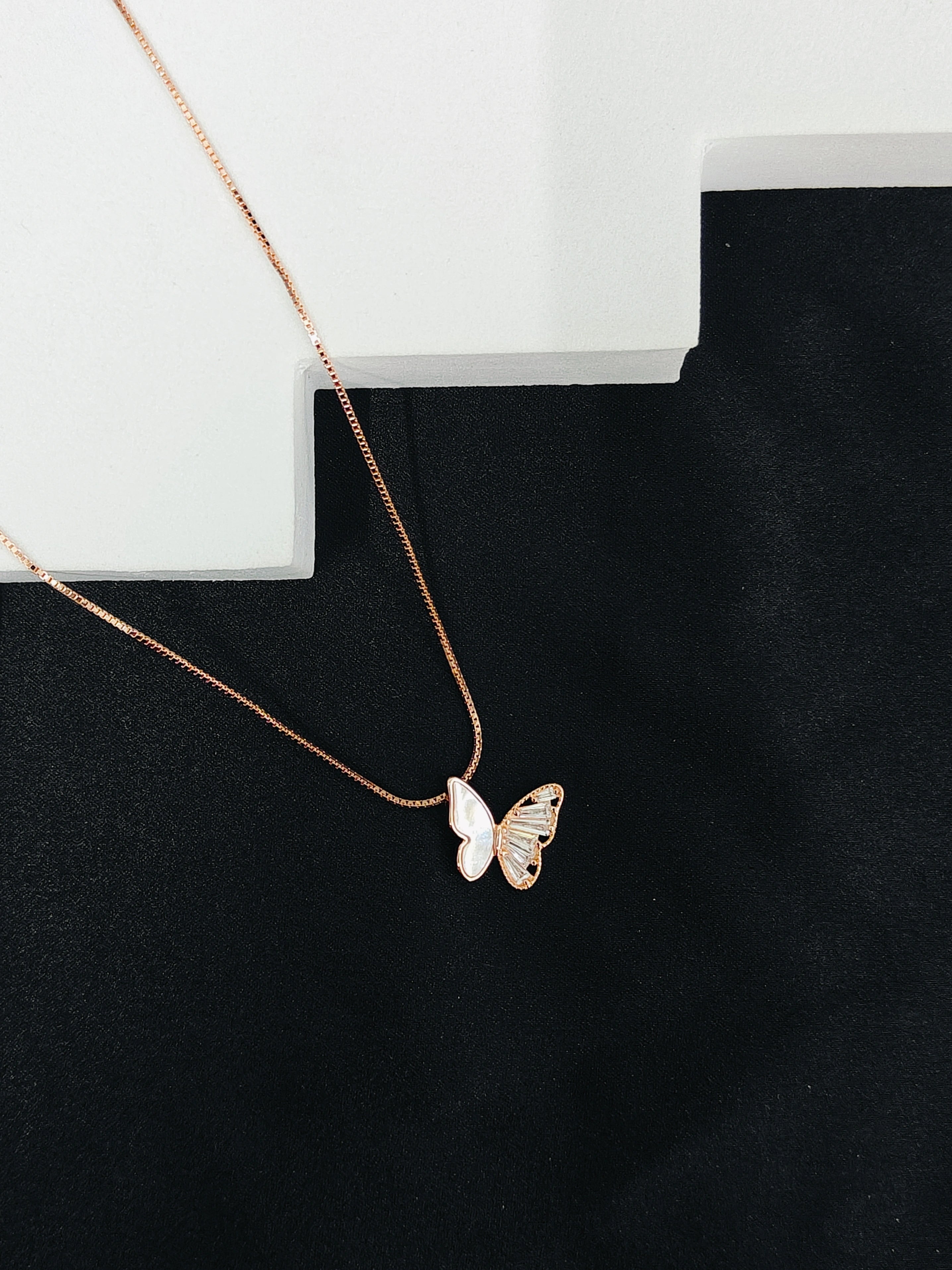 Butterfly pendant necklace on a black surface with a white block in the background
