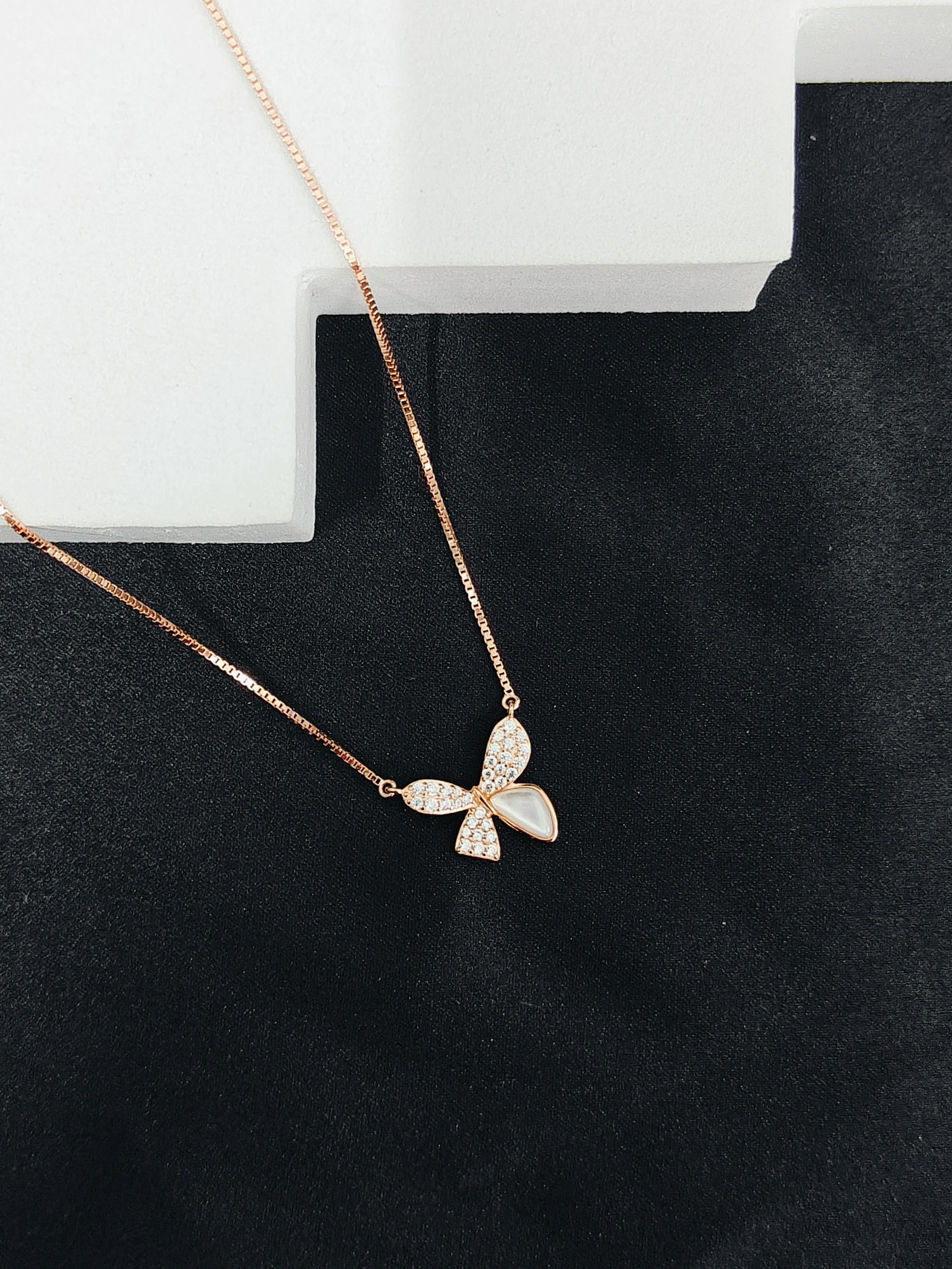 Rose gold butterfly necklace on a black surface with a white box in the background