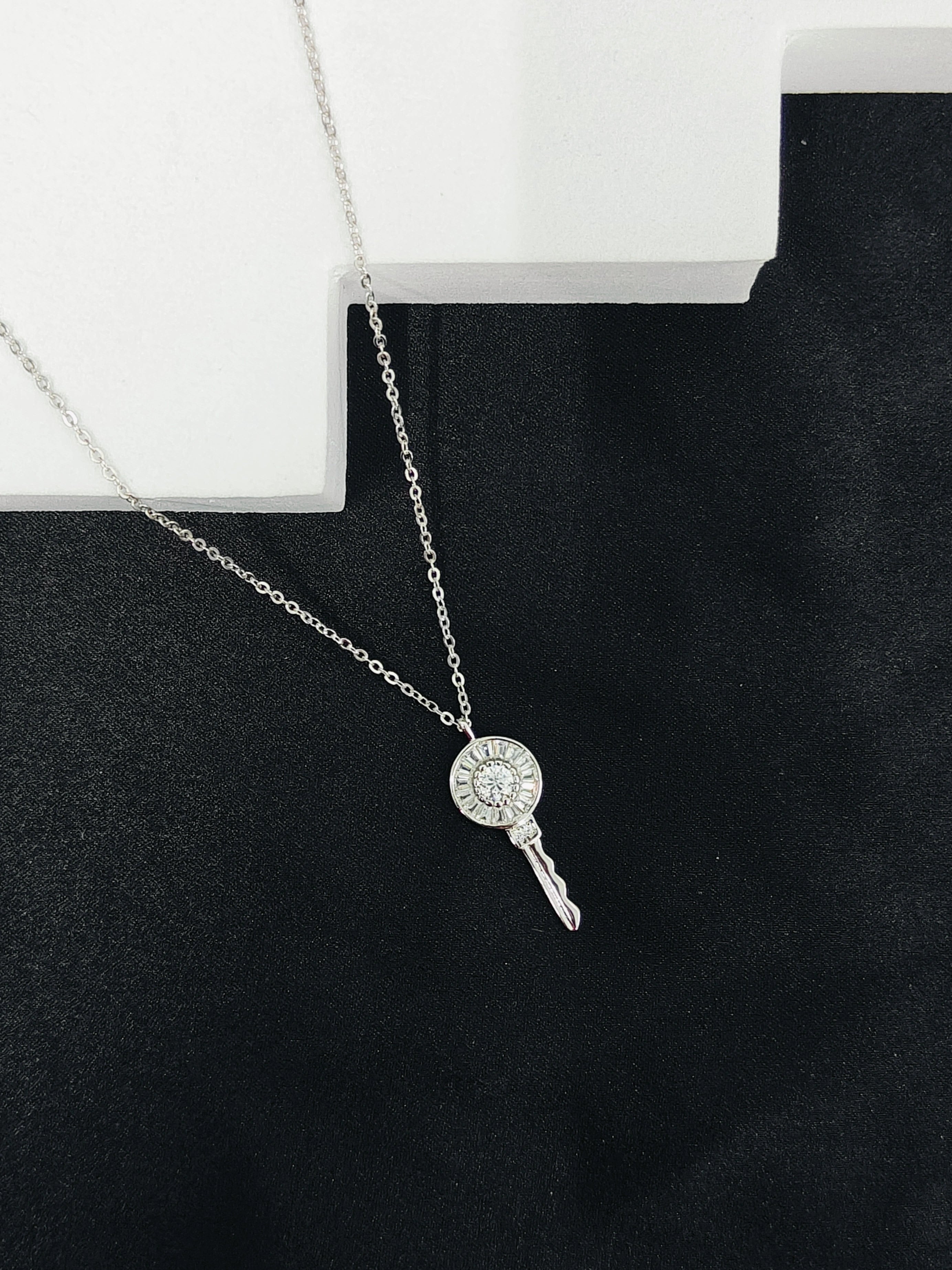 Silver key-shaped pendant necklace on a black surface with a white box in the background