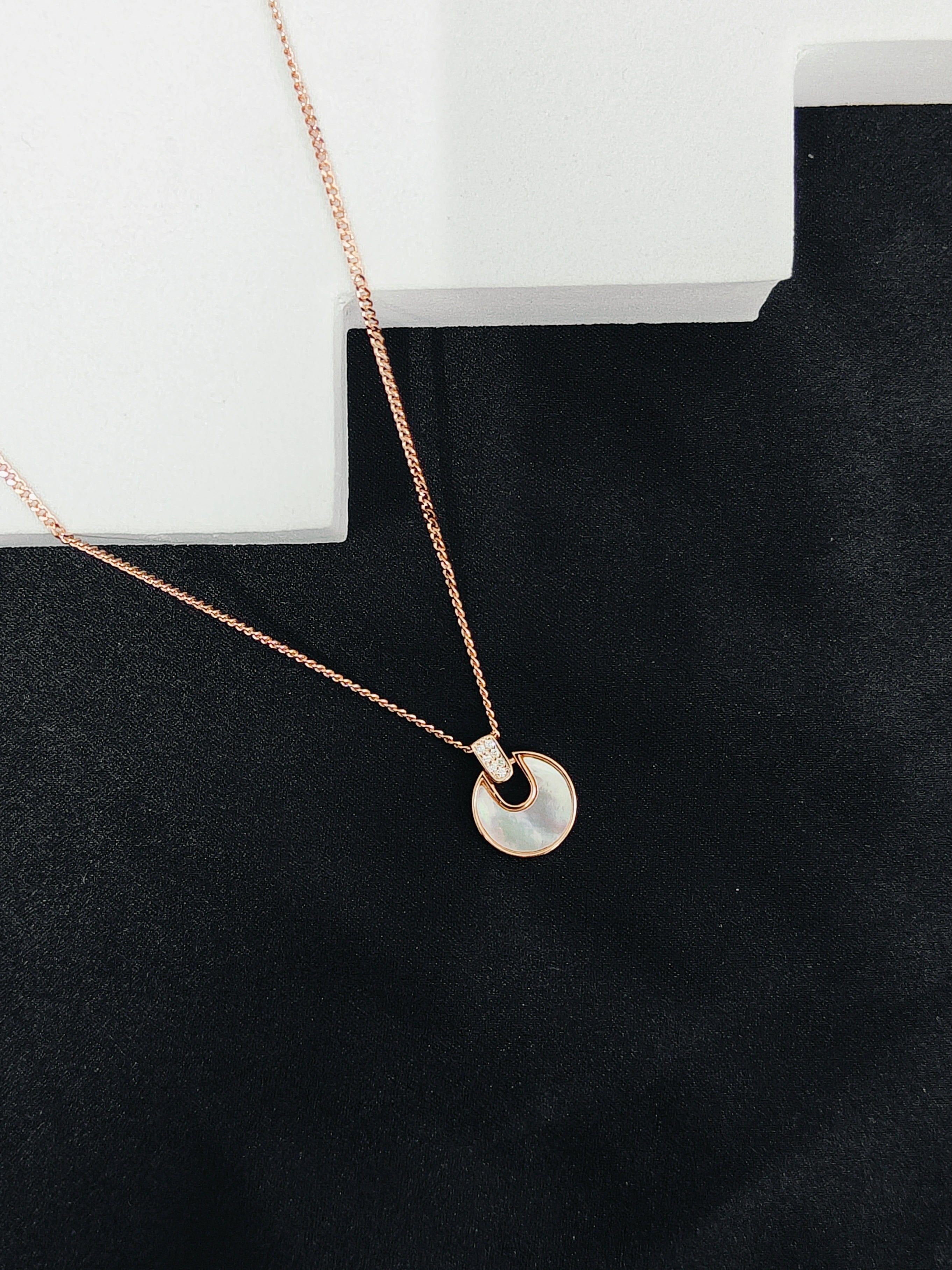 Rose gold necklace with a circular pendant on a black surface