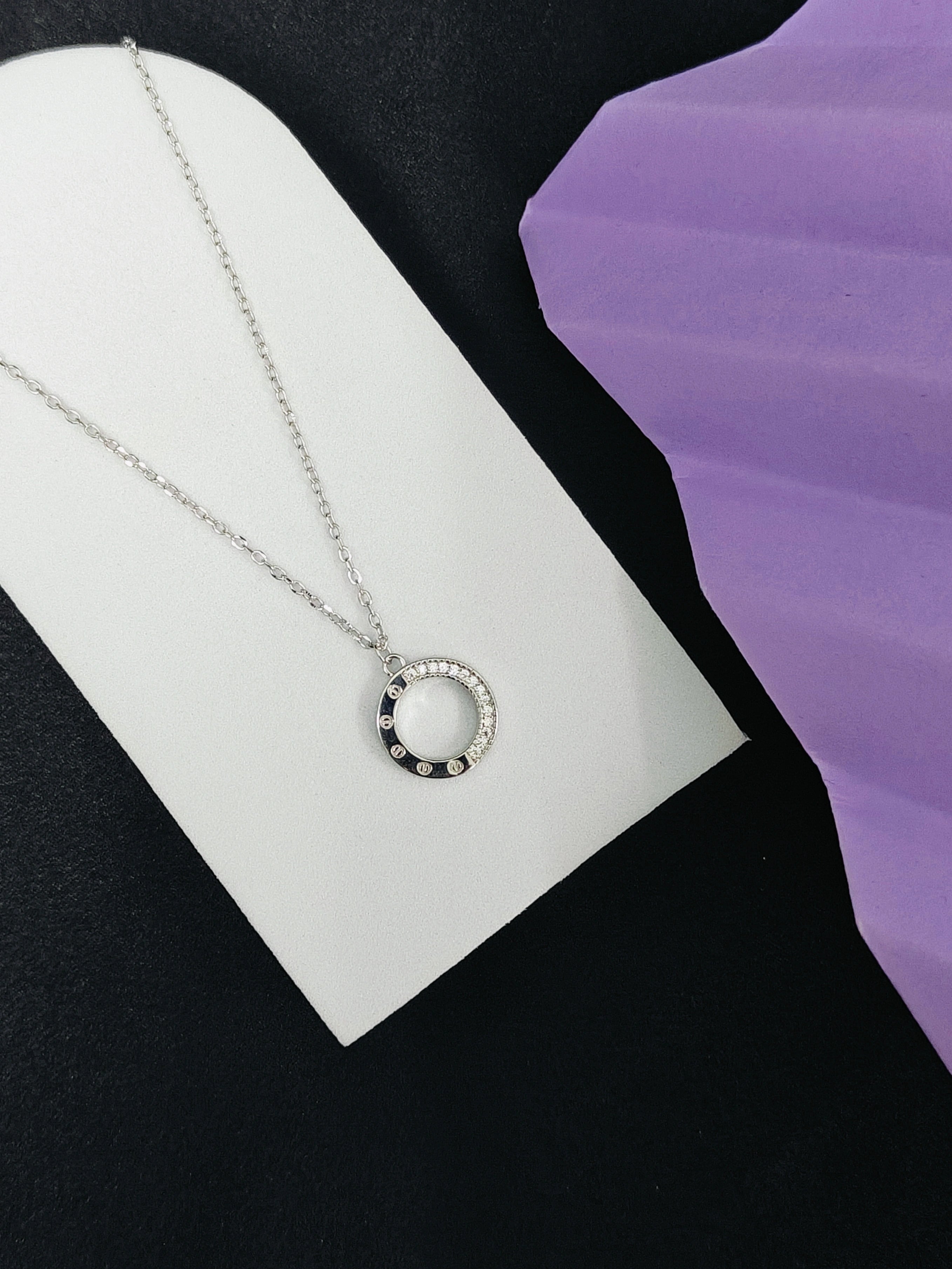 Silver necklace with a circular pendant on a white card against a black and purple background