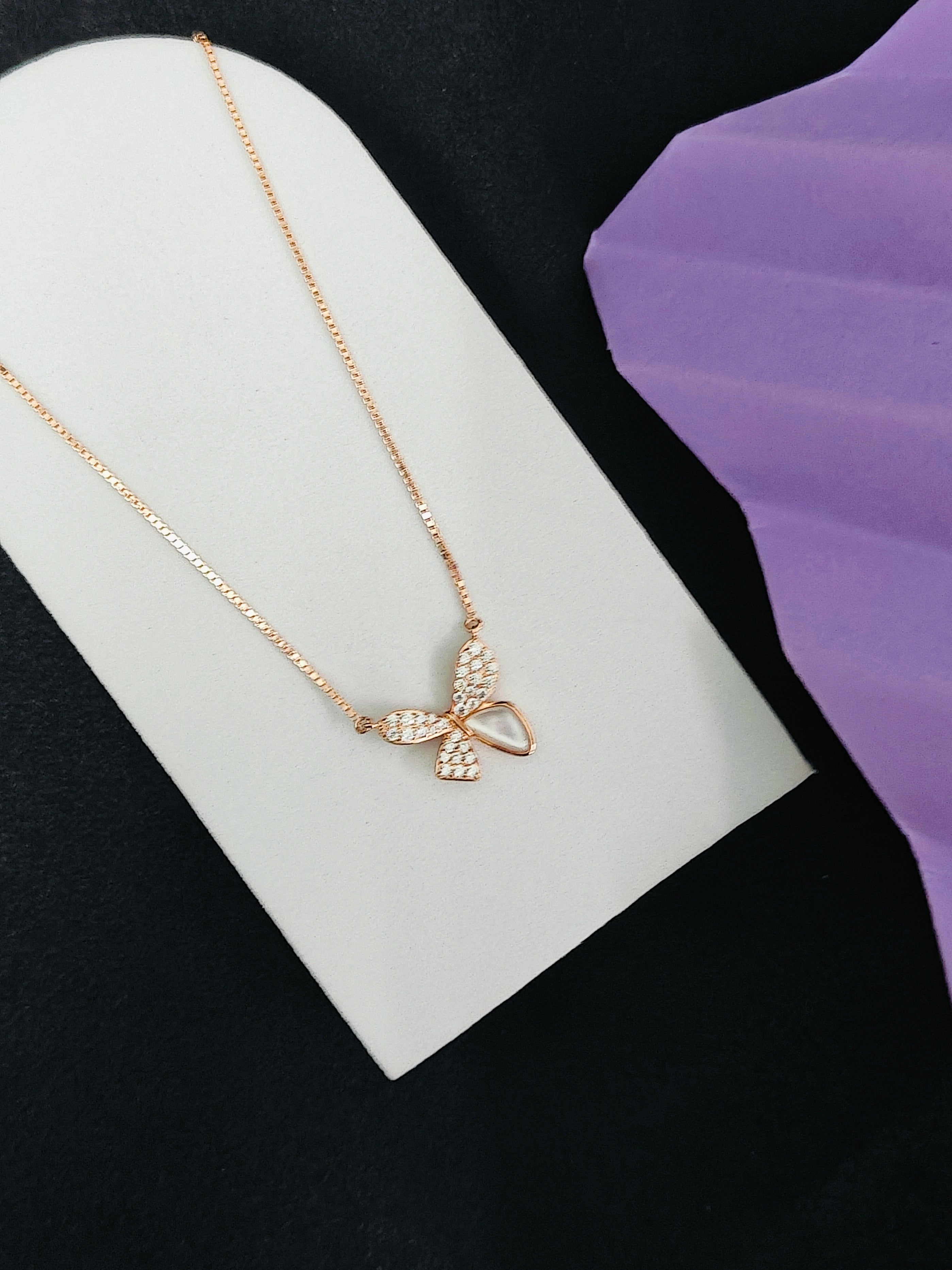 Rose gold necklace with a bow pendant on a white stand against a black background