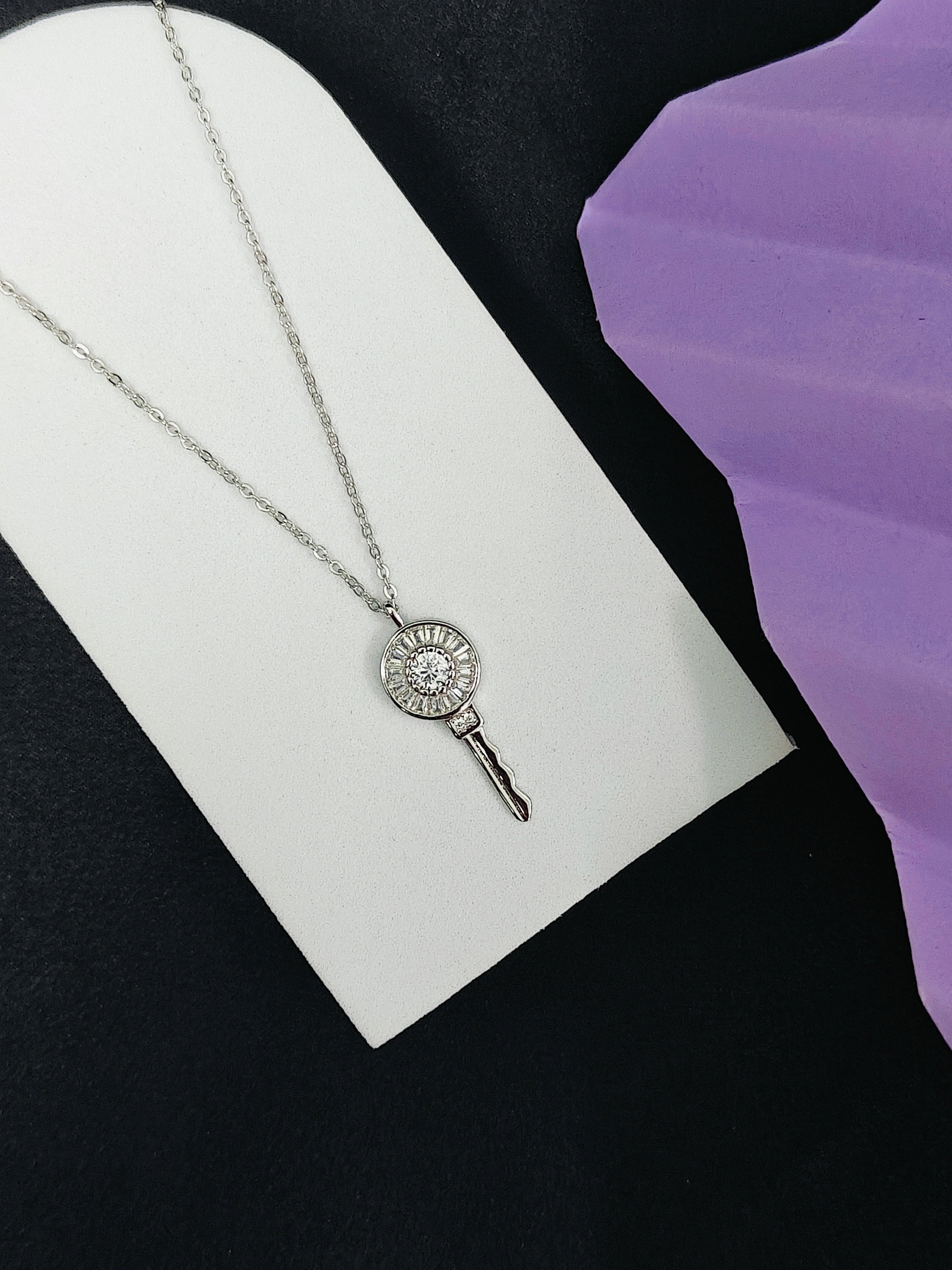 Silver necklace with a circular pendant on a white card against a black and purple background