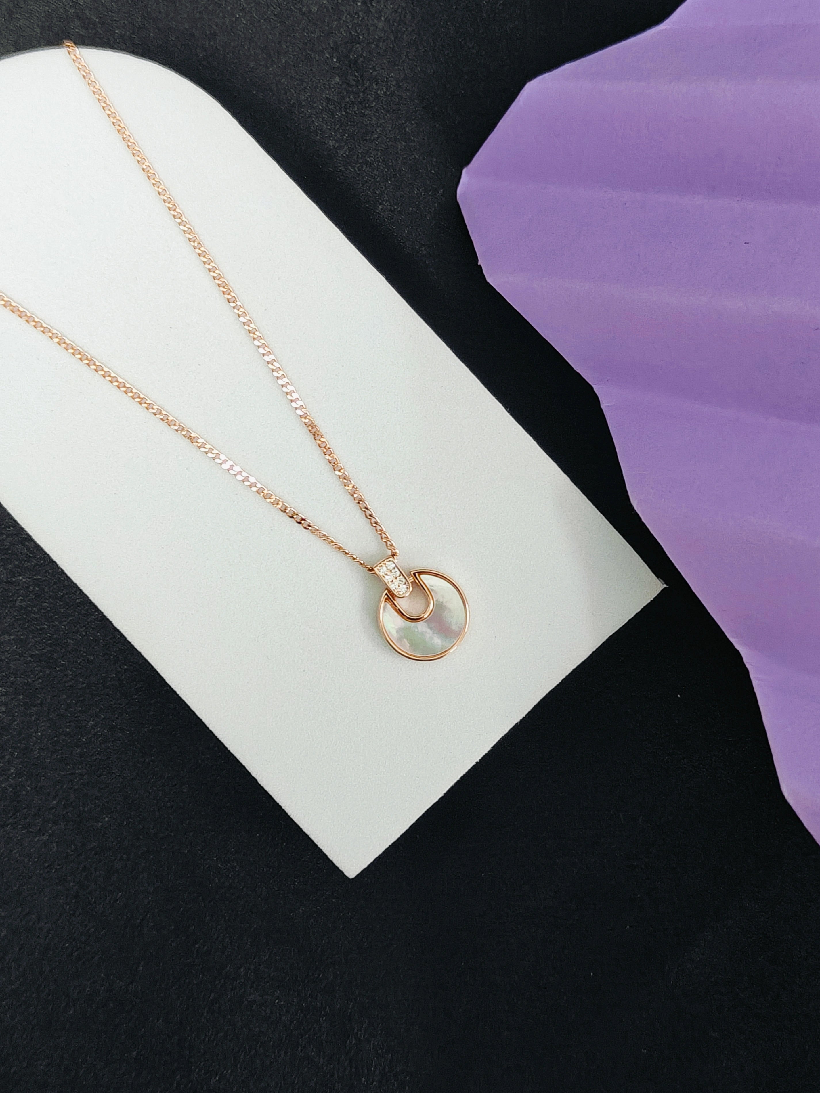 Gold necklace with a circular pendant on a white card against a black background