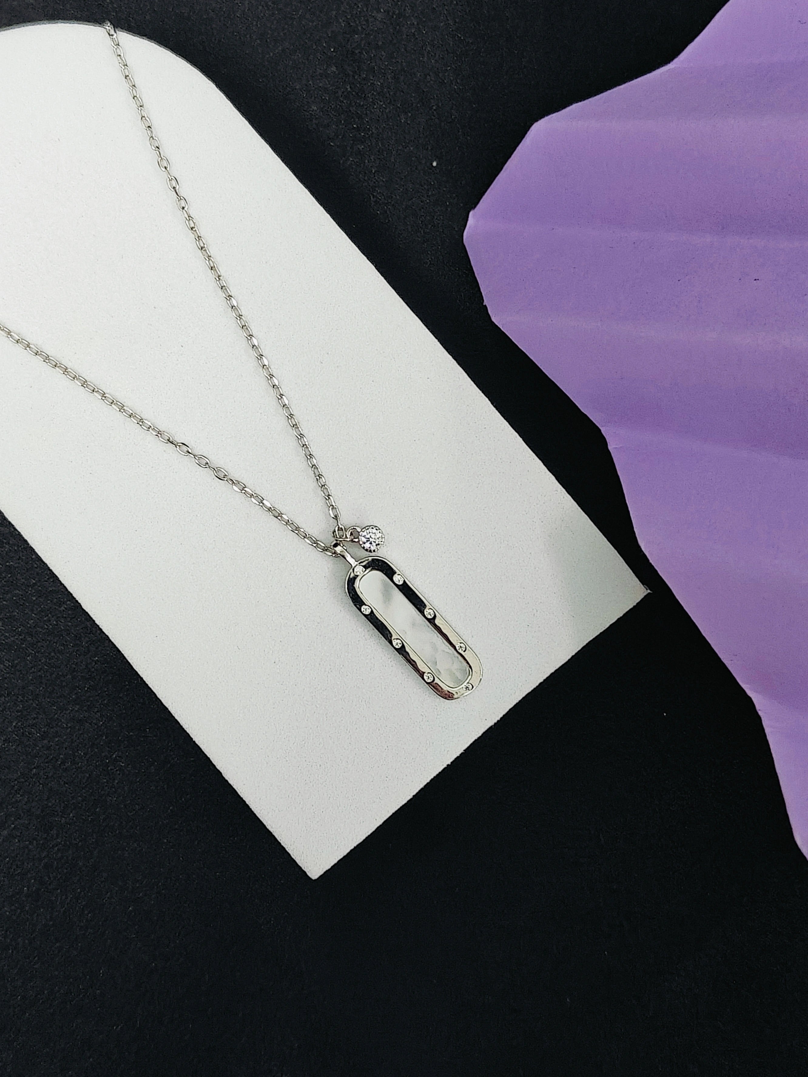 Silver necklace with a pendant on a white card against a black and purple background
