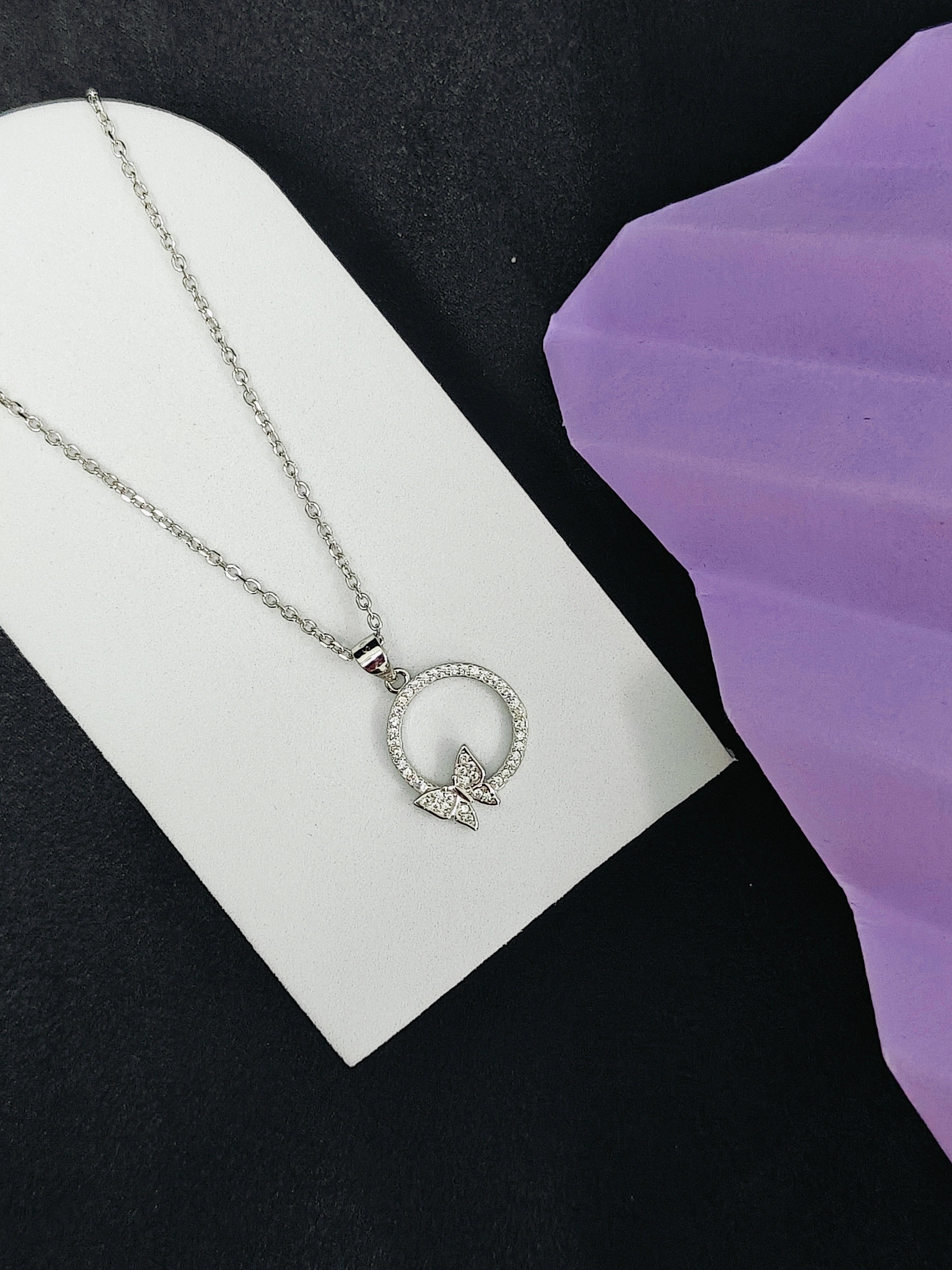 Silver necklace with a butterfly pendant on a white card against a black background