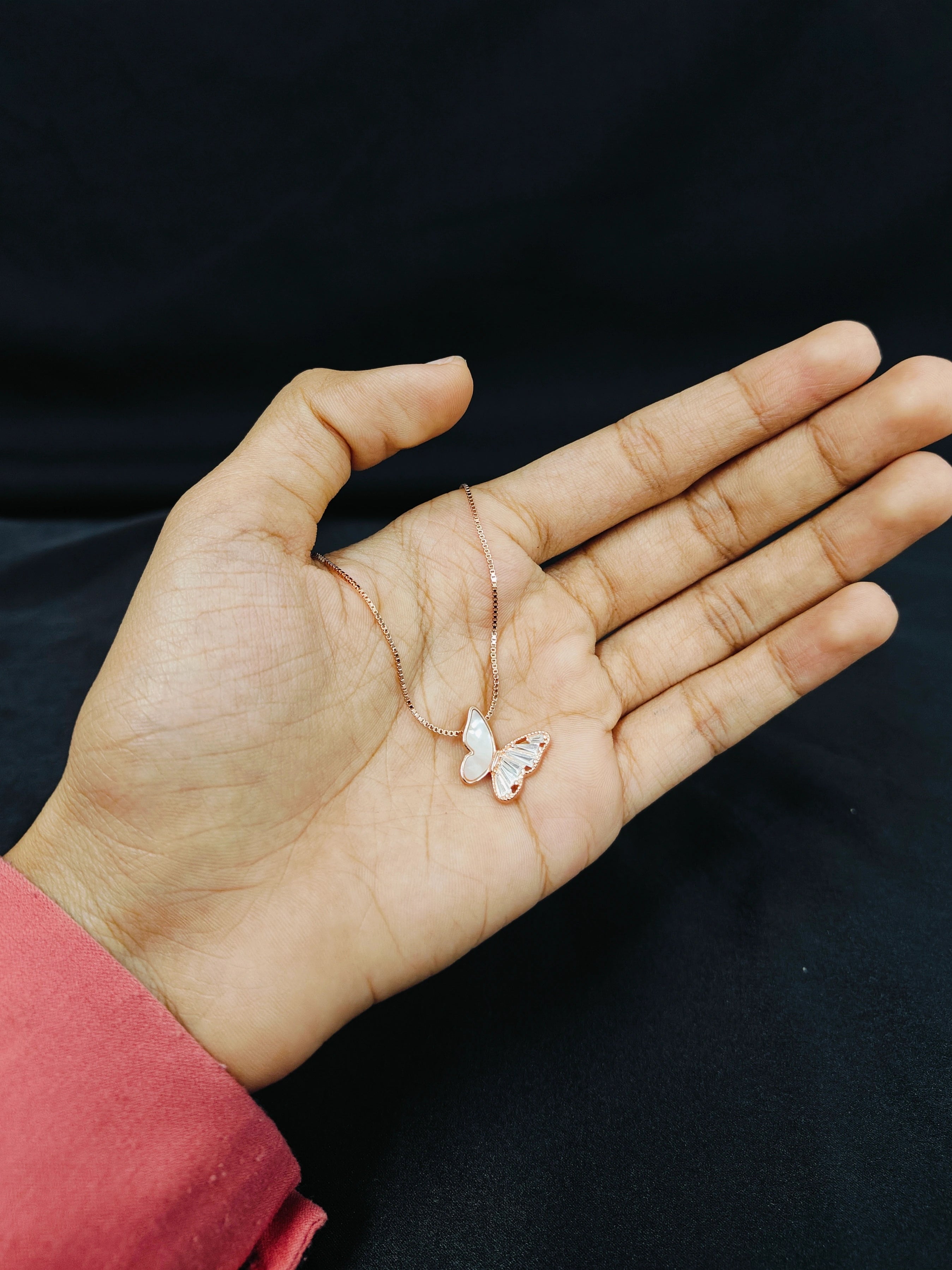 Hand holding a delicate necklace with butterfly pendant against a dark background