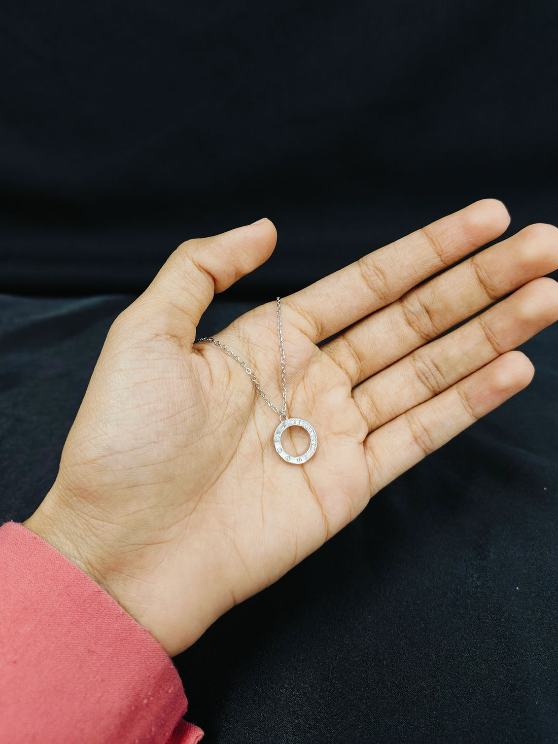 Hand holding a delicate necklace with a circular pendant against a black background
