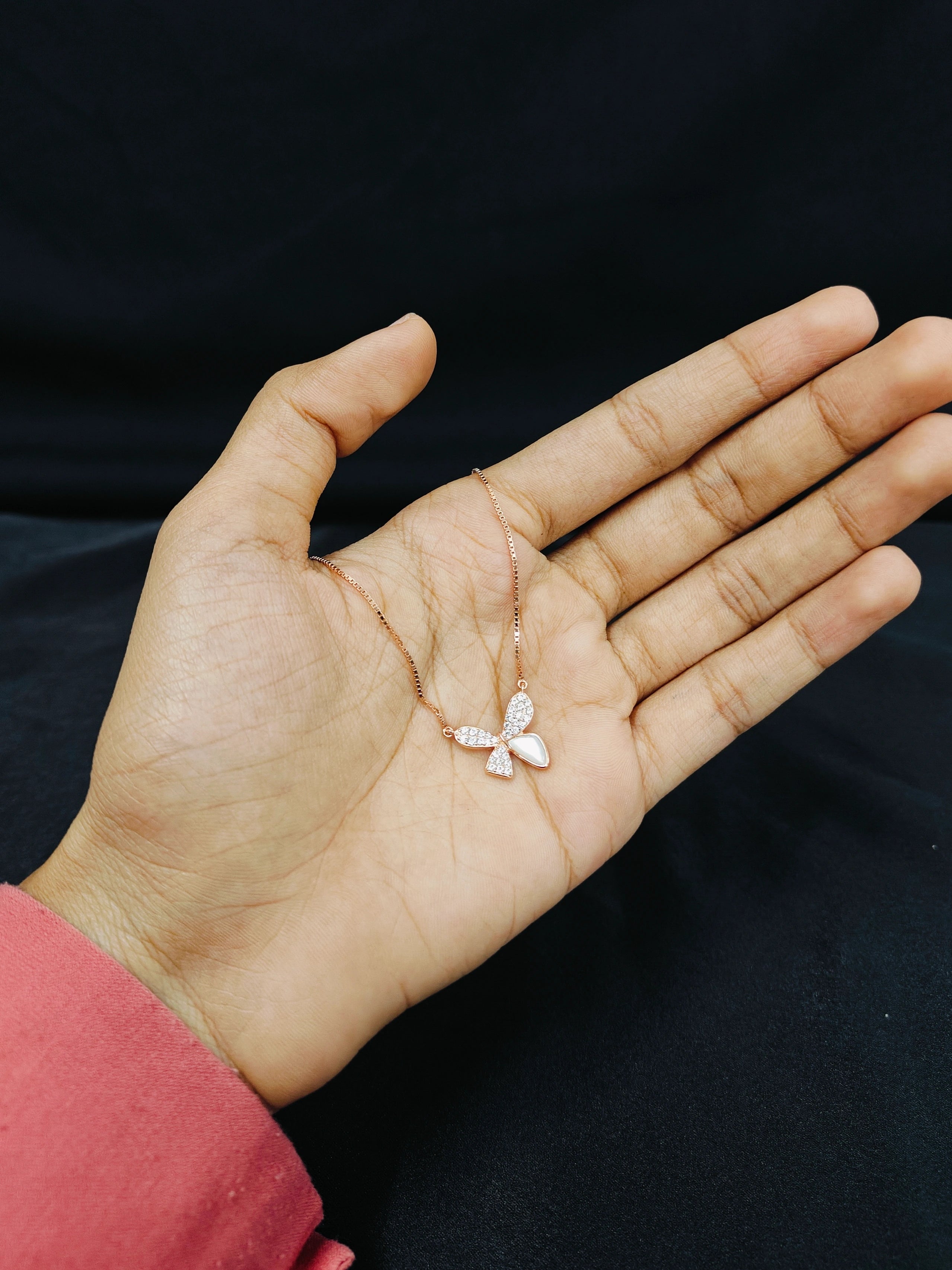 Hand holding a delicate butterfly necklace against a black background