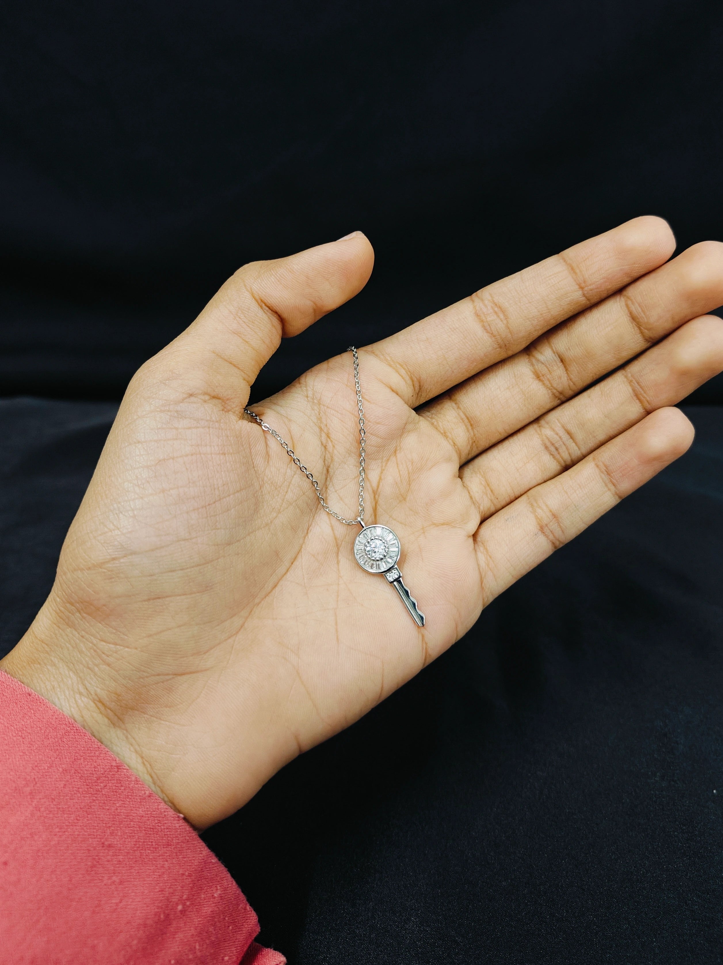 Hand holding a delicate necklace with a clear pendant against a black background