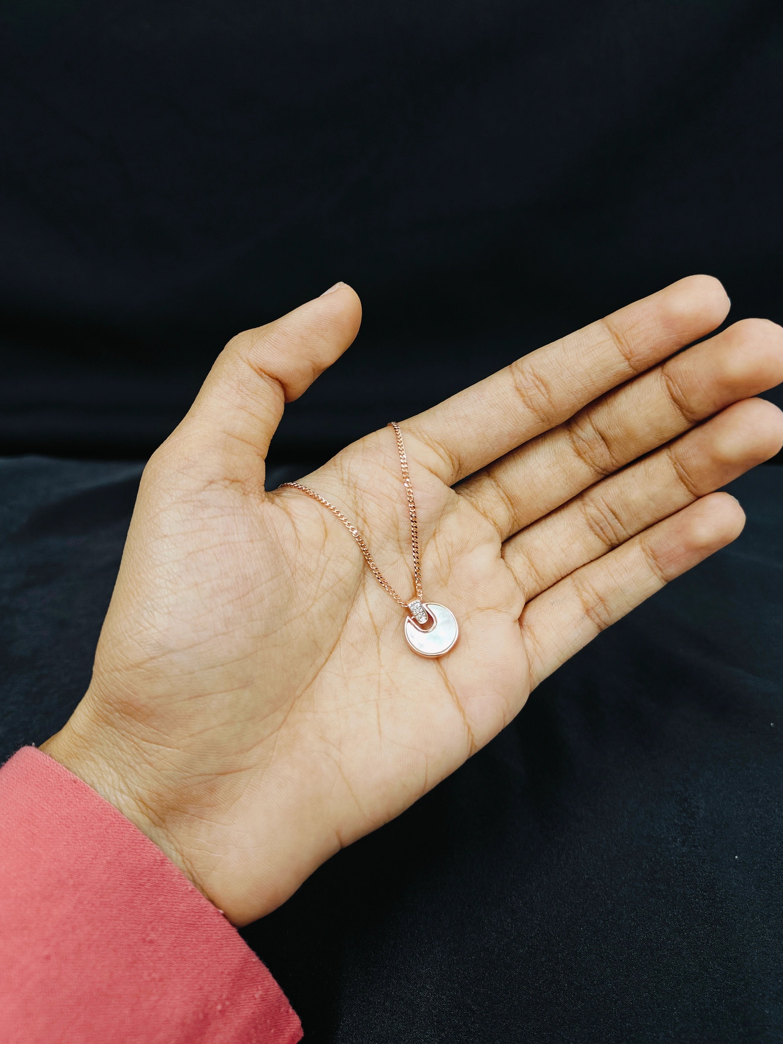 Hand holding a necklace with a small pendant against a dark background