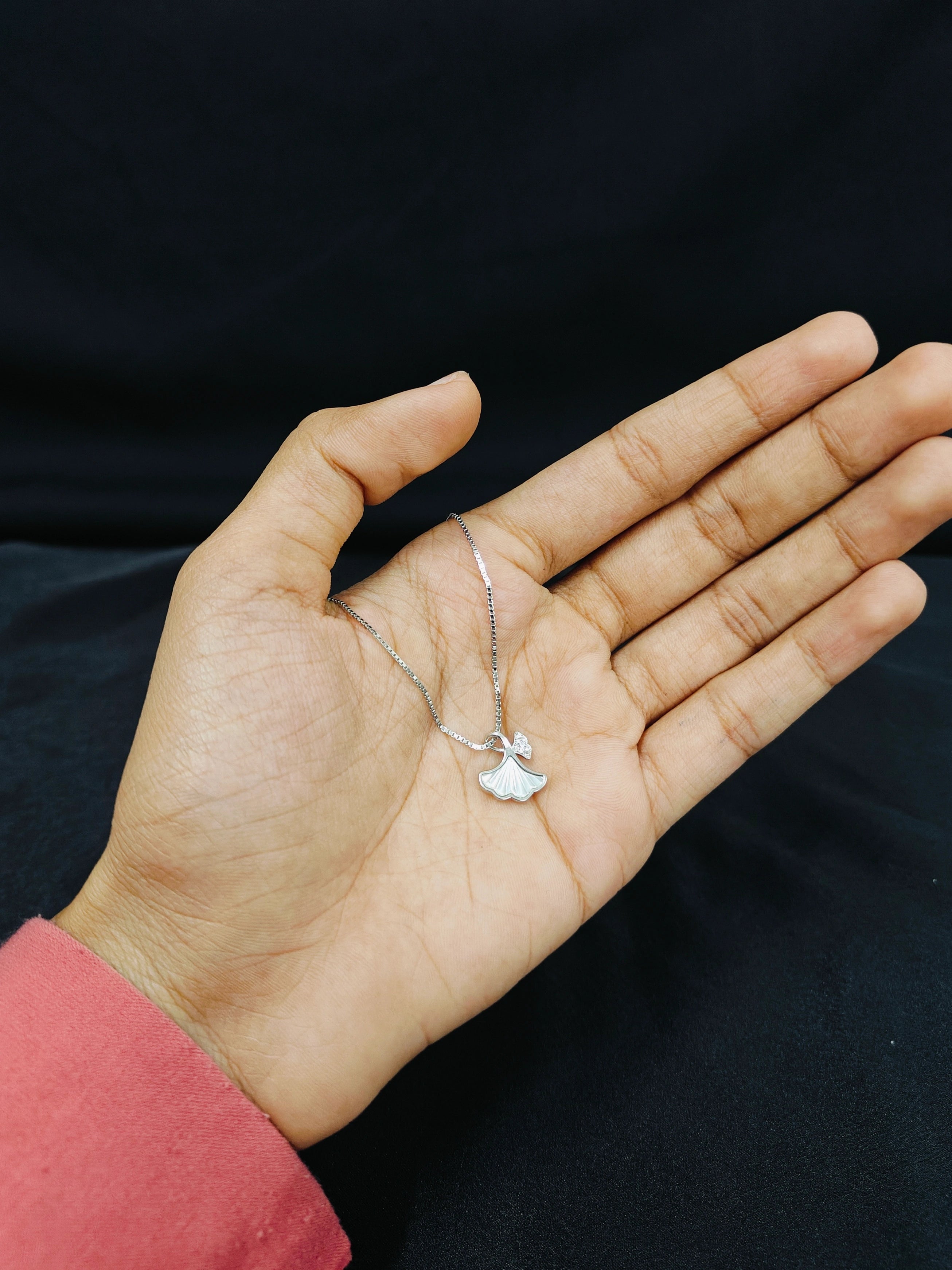Hand holding a delicate silver necklace with a small pendant against a black background
