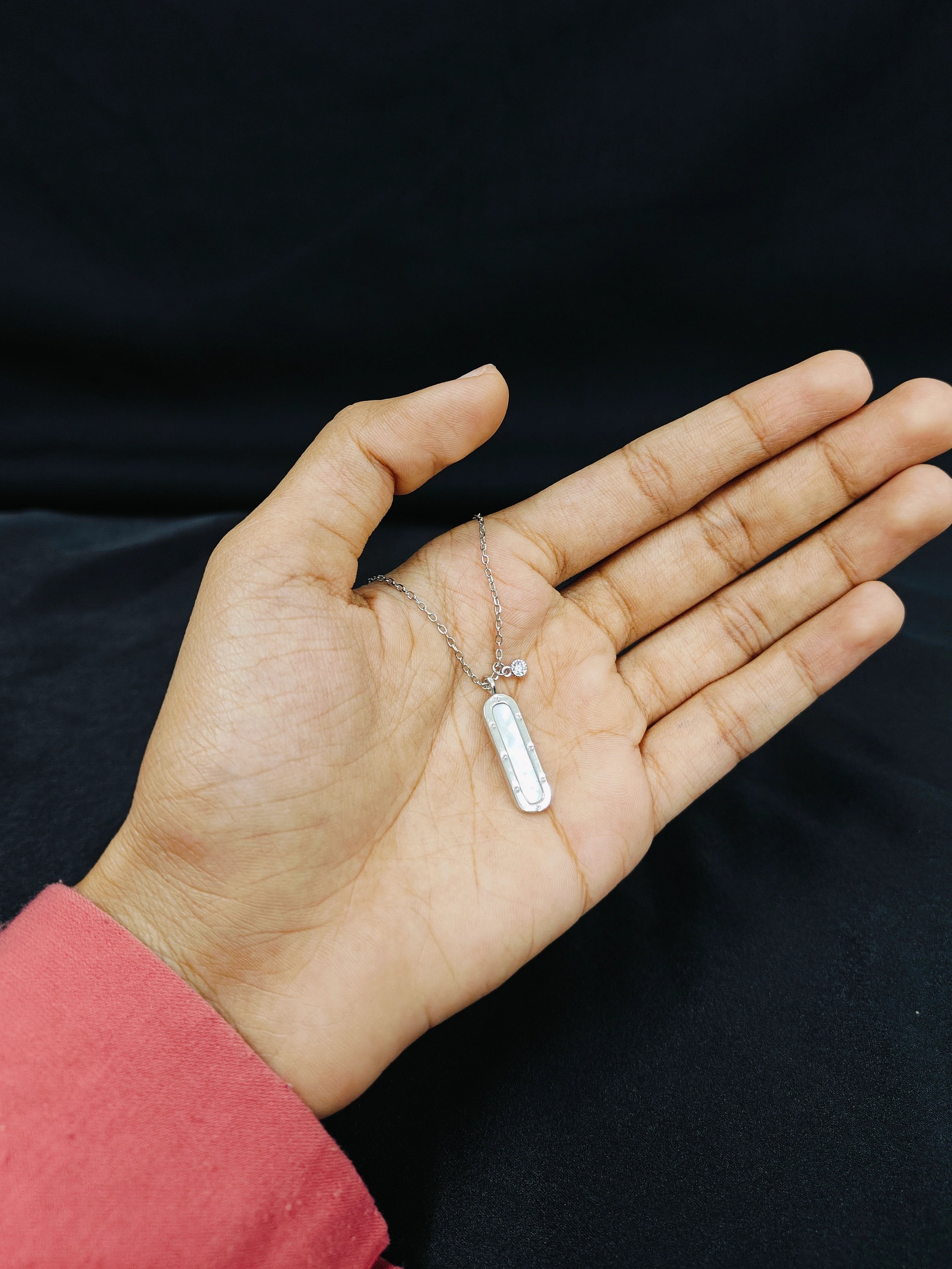 Hand holding a silver necklace with a tag against a black background