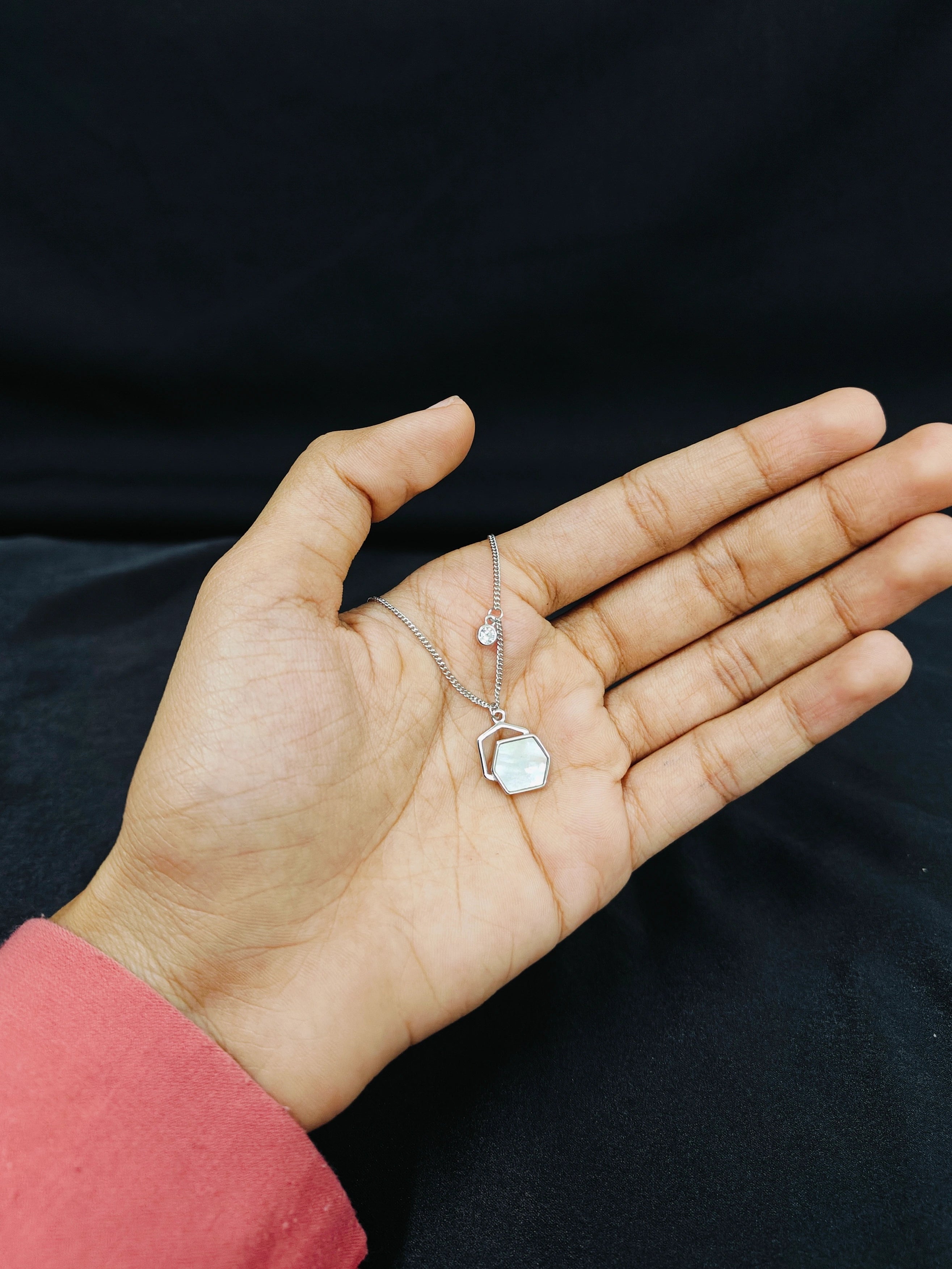 Hand holding a delicate necklace with a clear pendant against a dark background