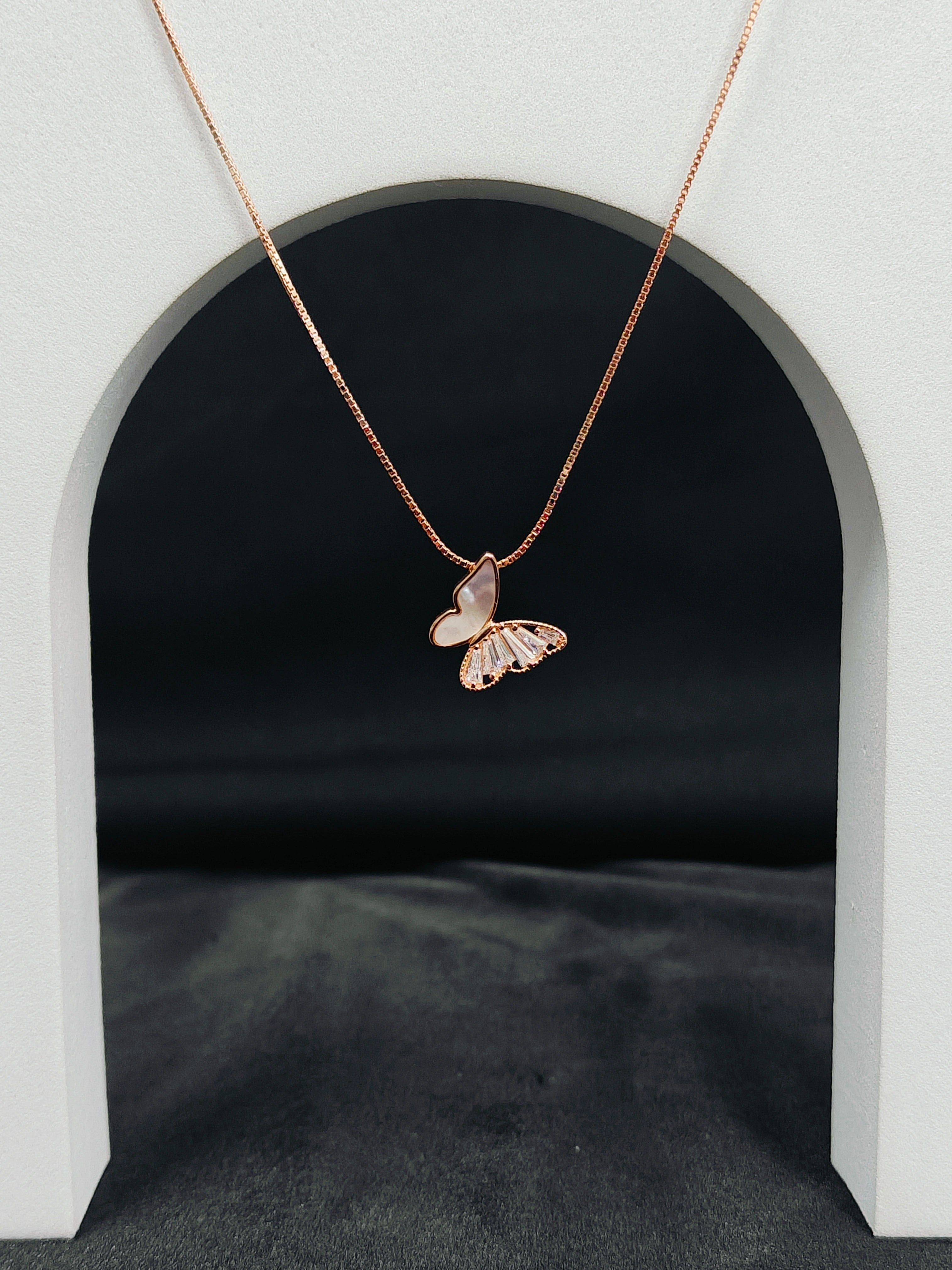 Rose gold butterfly necklace on a gray background
