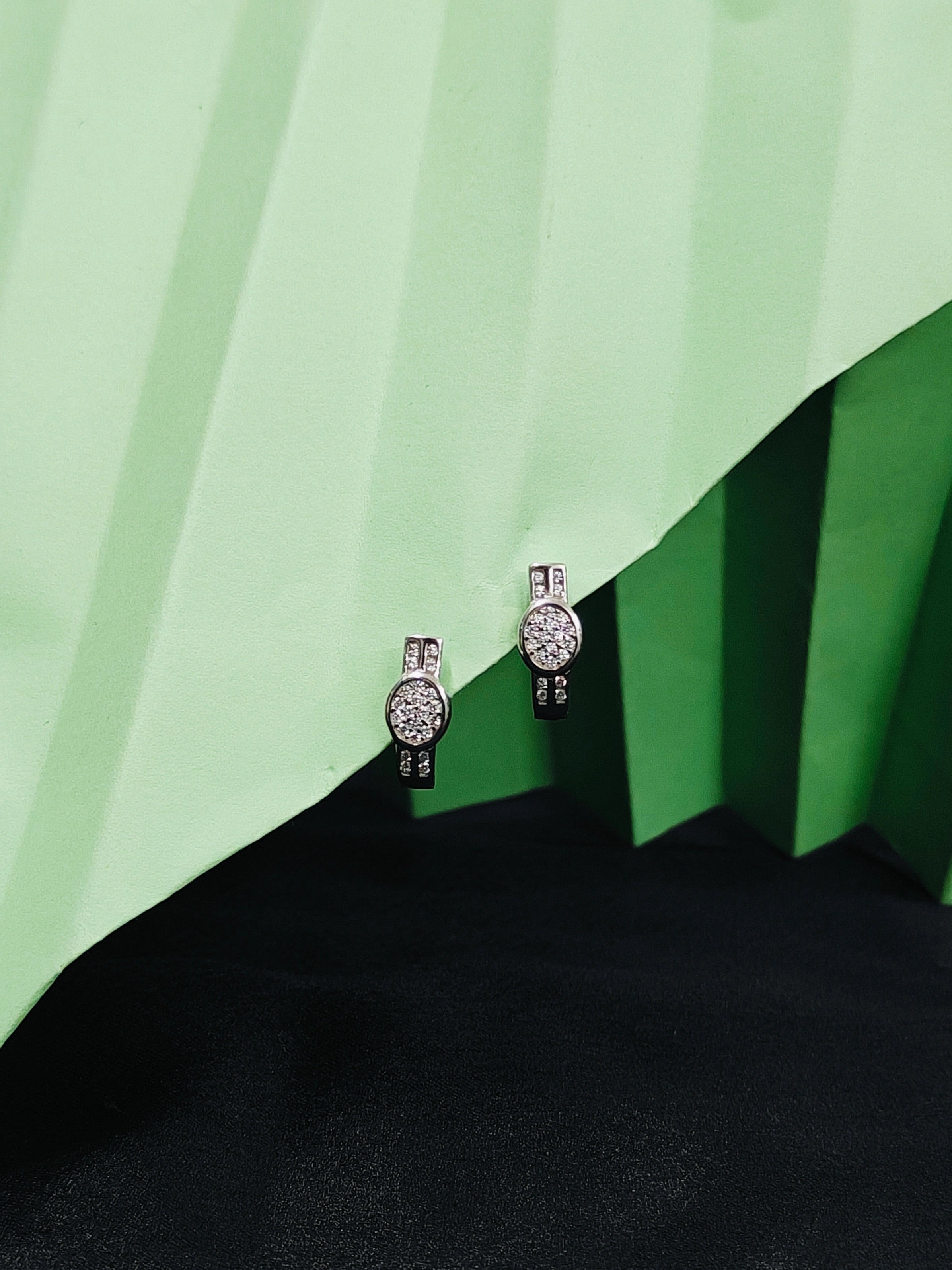 Pair of silver earrings with clear stones on a green and black background