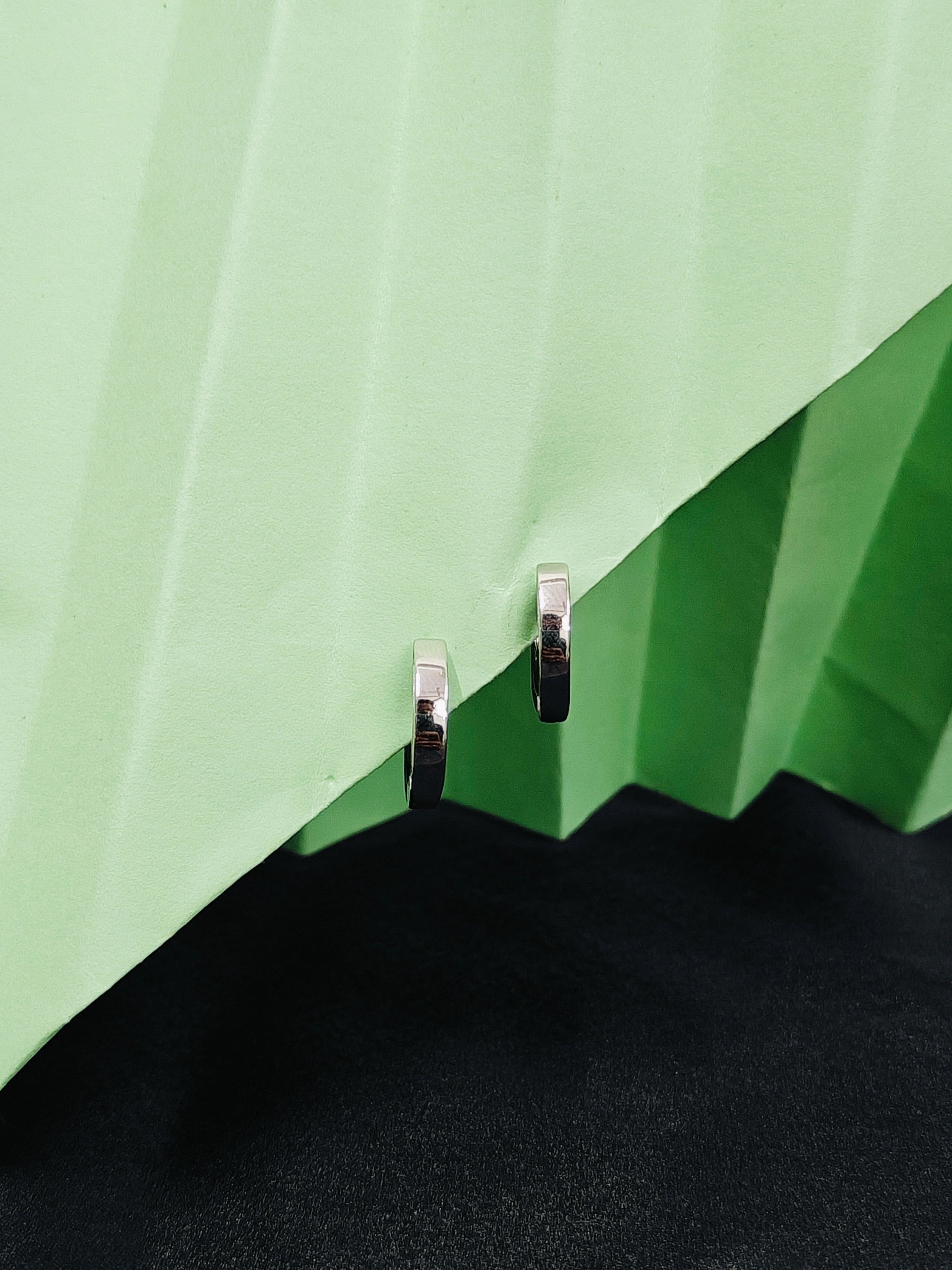Close-up of a green umbrella with a black handle and silver clips on a light green background.